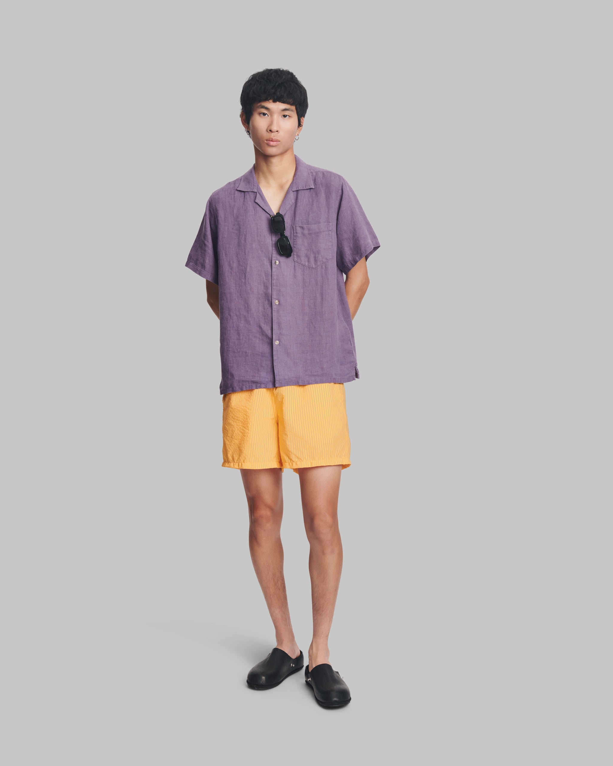 Person wearing a purple shirt and yellow shorts on a gray background