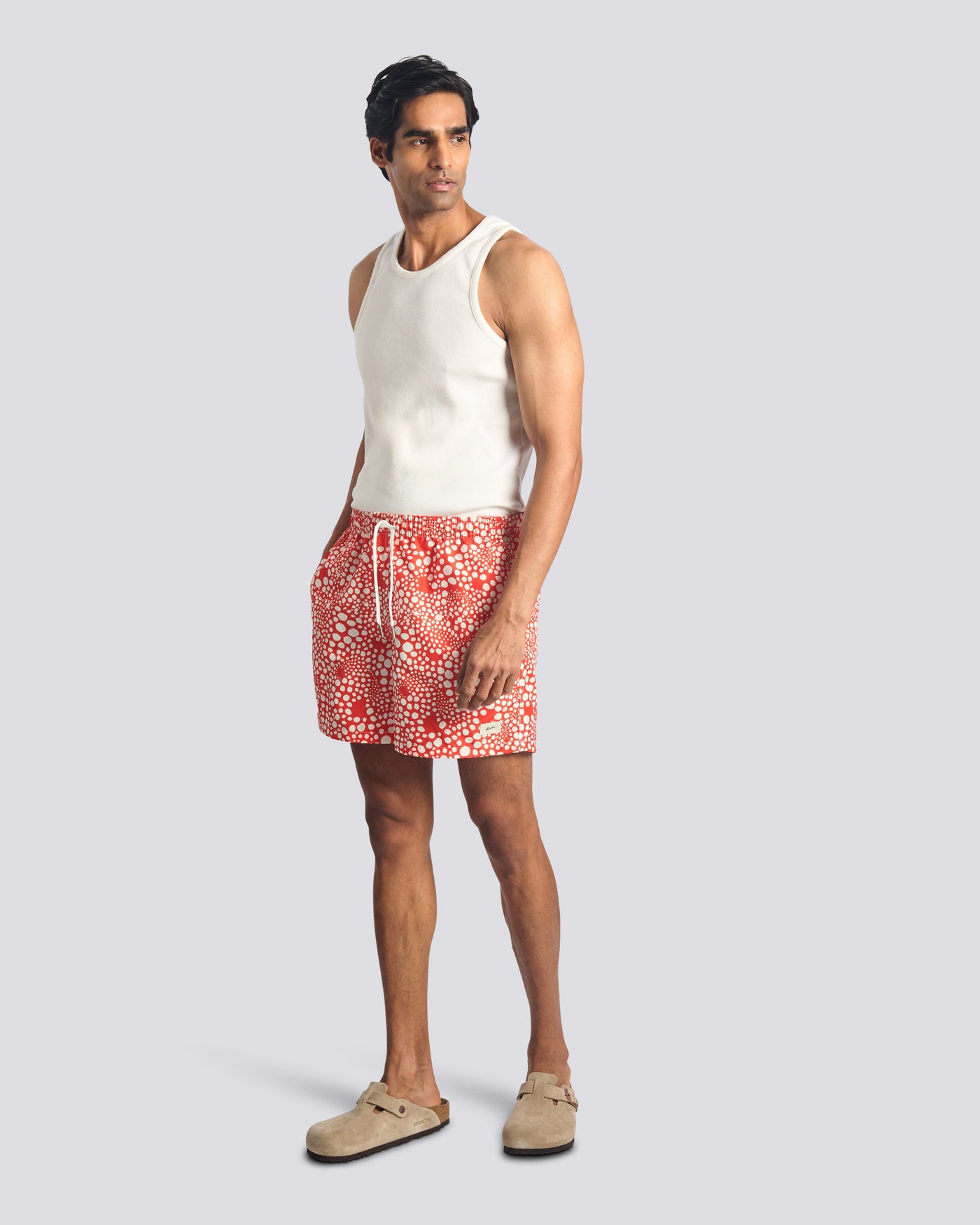 Man wearing a white sleeveless shirt and red patterned shorts on a light gray background