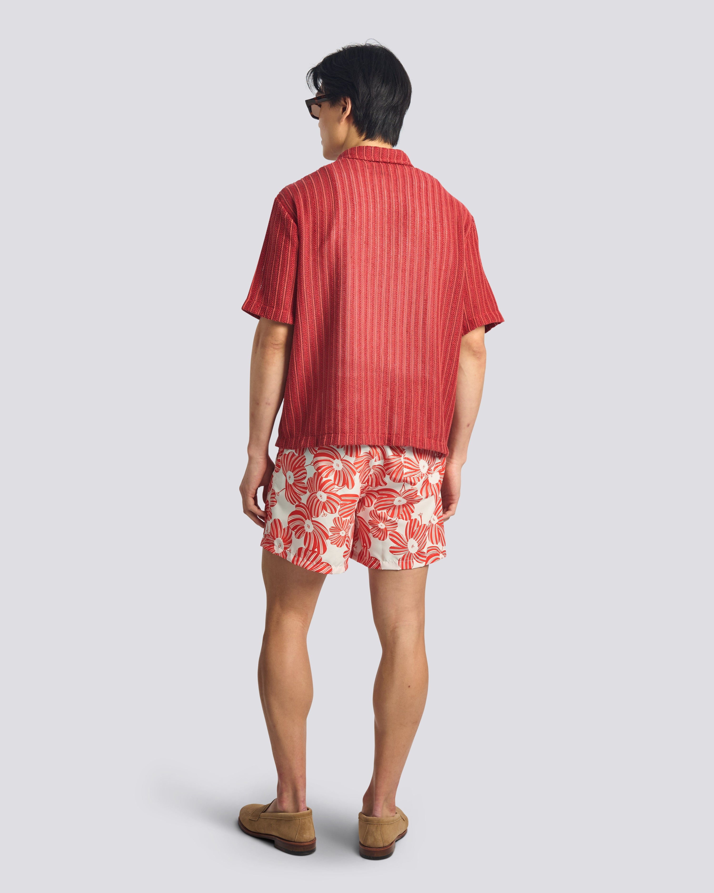 Person wearing a red striped shirt and red floral shorts on a light gray background