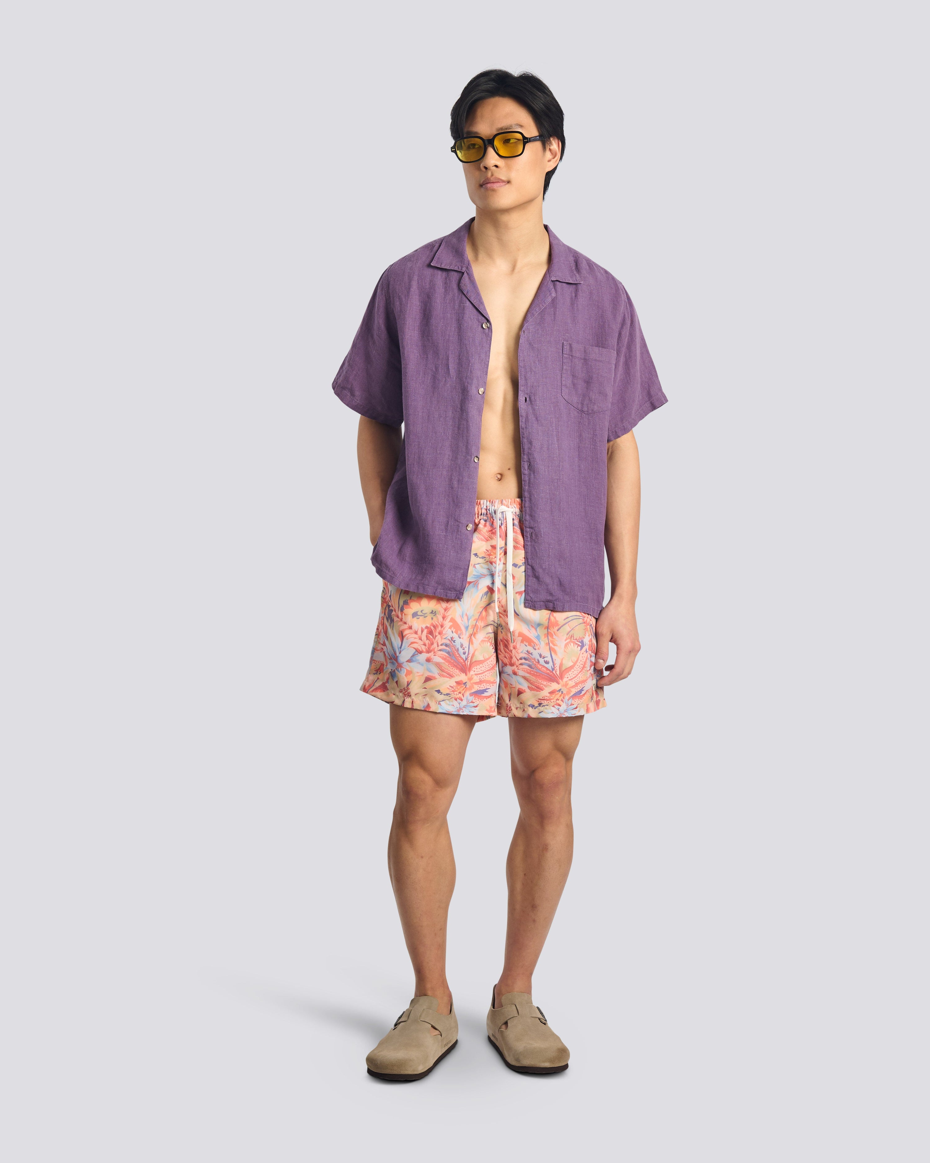 Man wearing a purple shirt and colorful shorts on a plain background