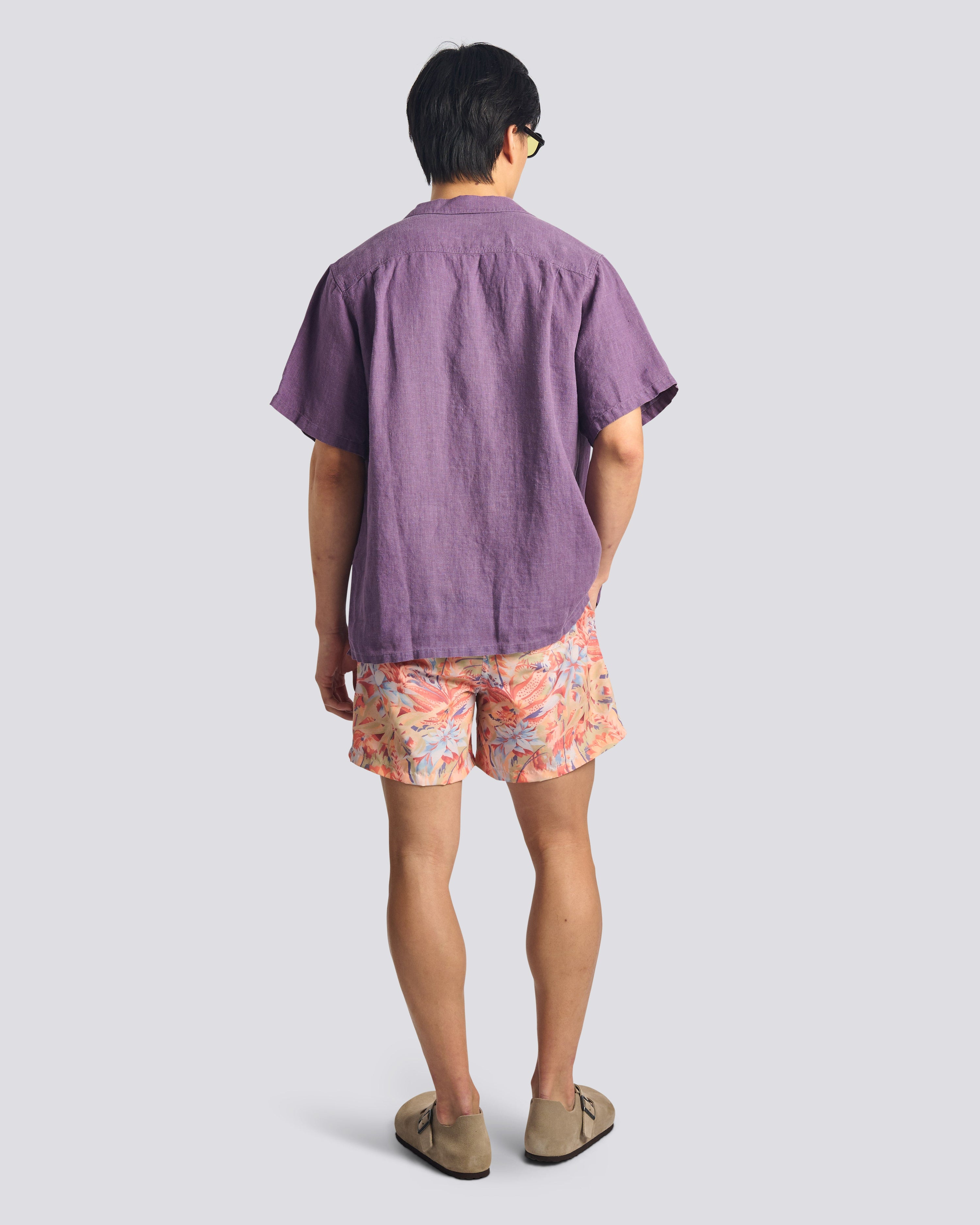 Person wearing a purple shirt and floral shorts on a plain background