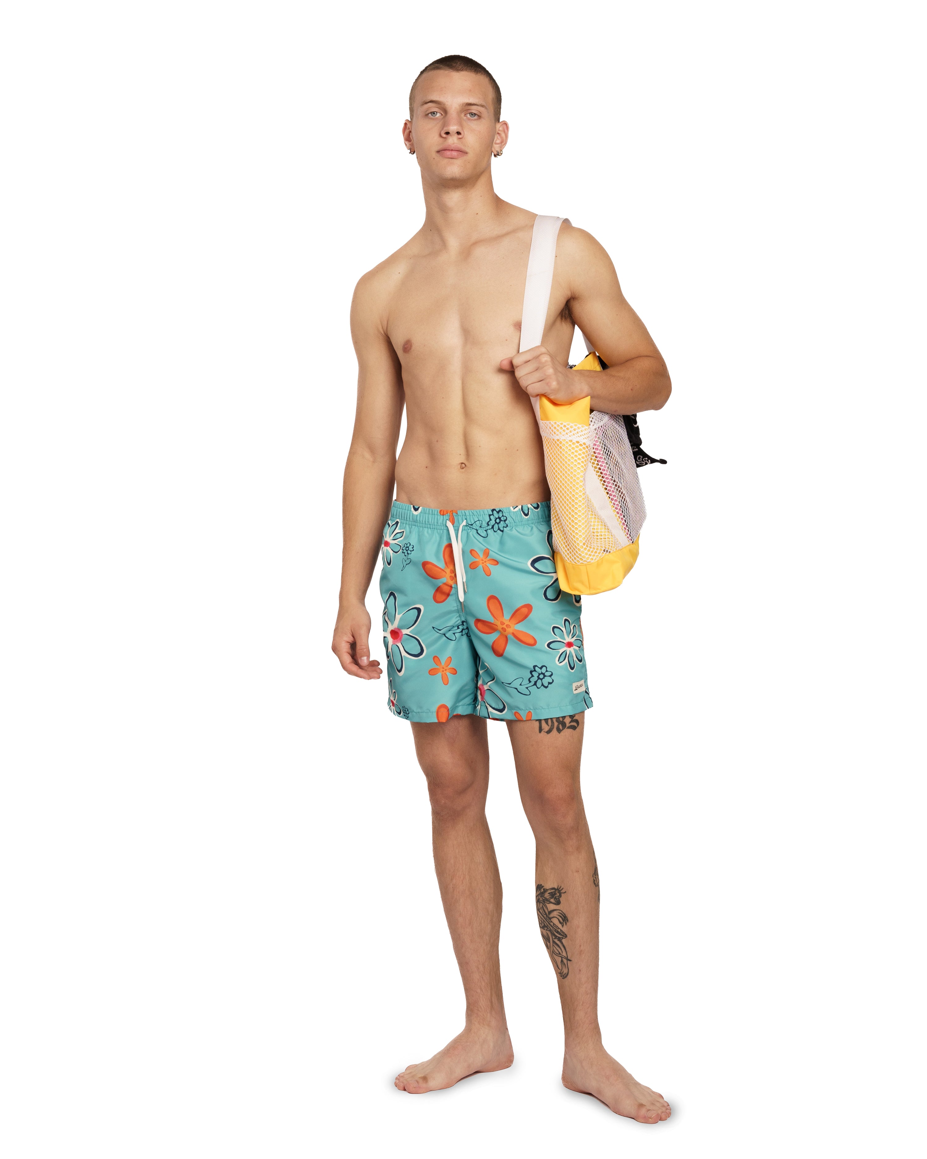 Model wearing Blue Bather swim trunk with floral pattern and orange flowers