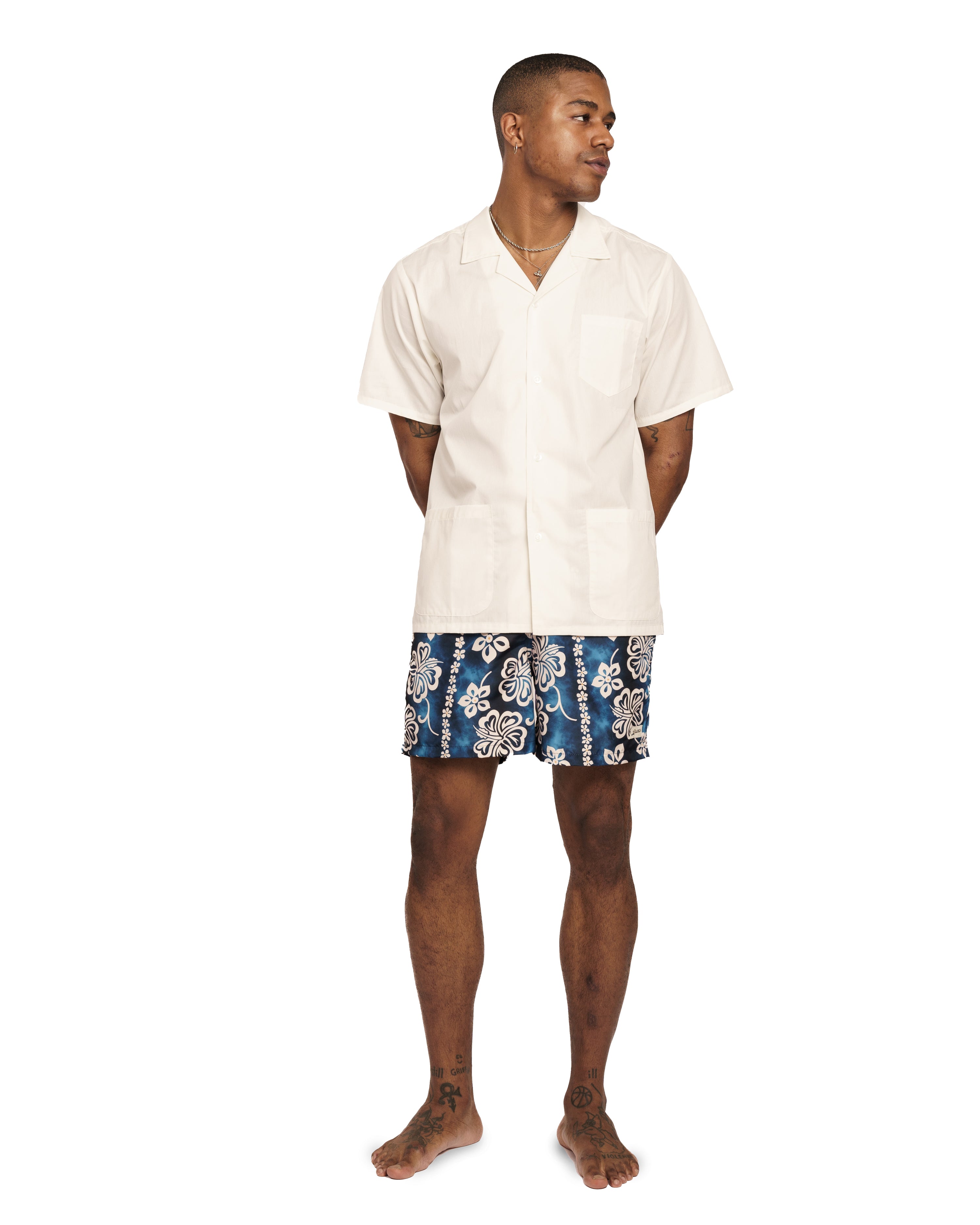 Model wearing Blue Bather swim trunk with a tropical pattern and beige floral motif