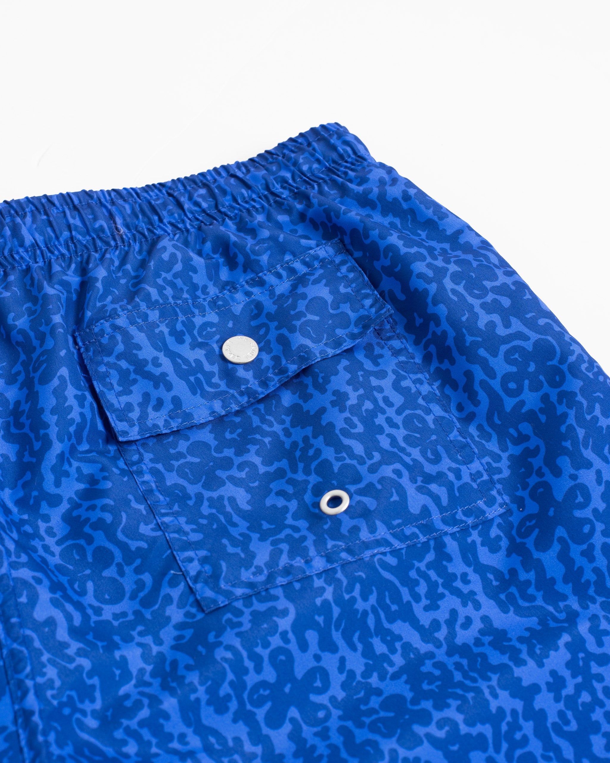 Close-up of back button-closure pocket on men’s blue camo swim trunks