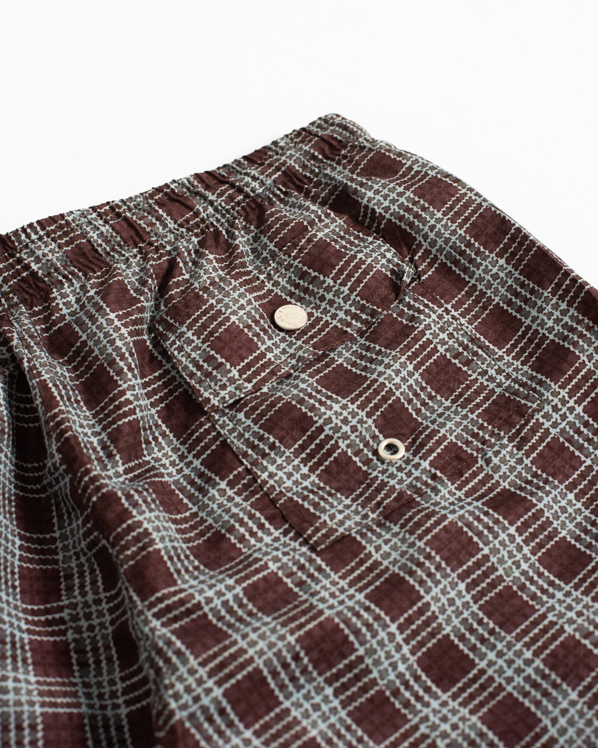 Close-up of the back button-closure pocket on Bather plaid swim trunks