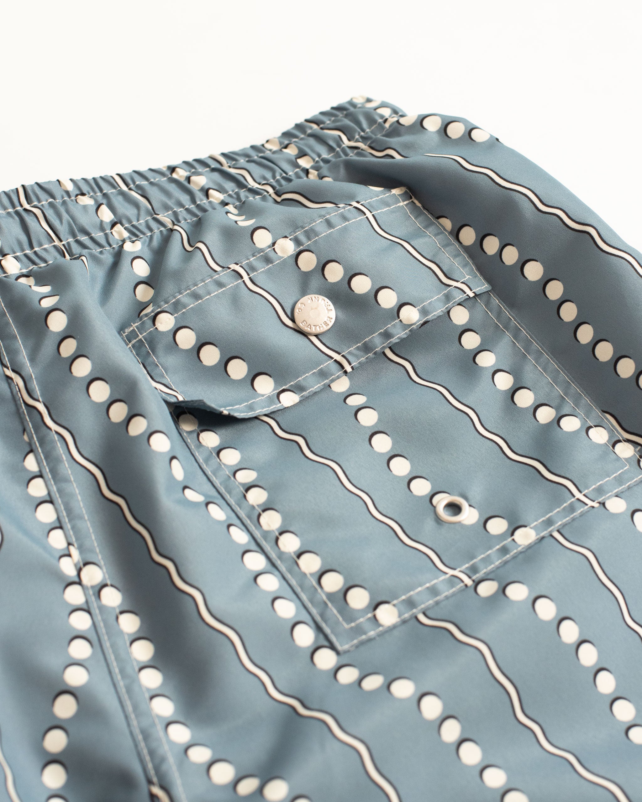 Close-up of the back button-closure pocket on men’s blue swim trunks with white dot and wavy stripe pattern