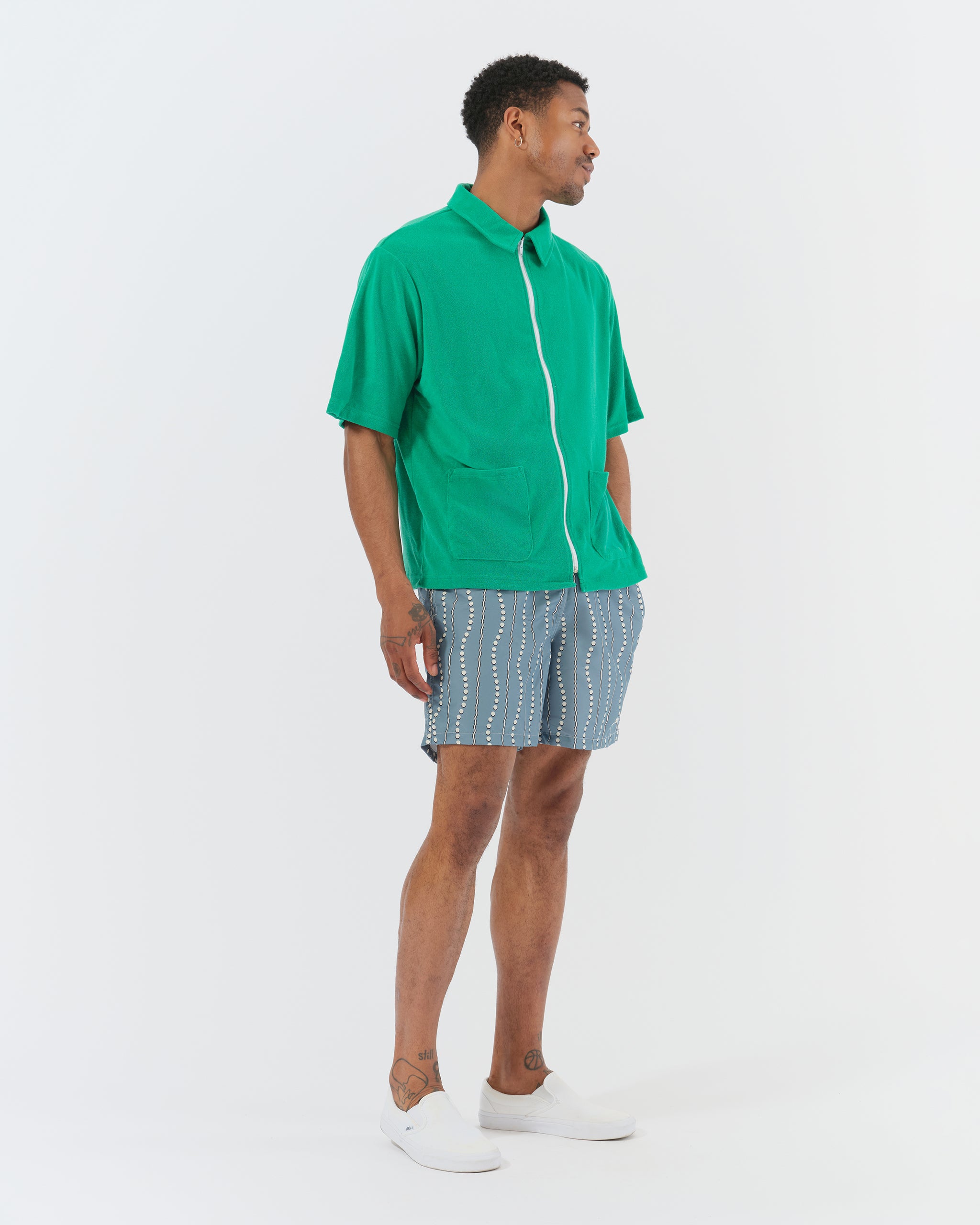 Man wearing Bather blue wavy dot print swim shorts and Bather green terry cloth zip-up
