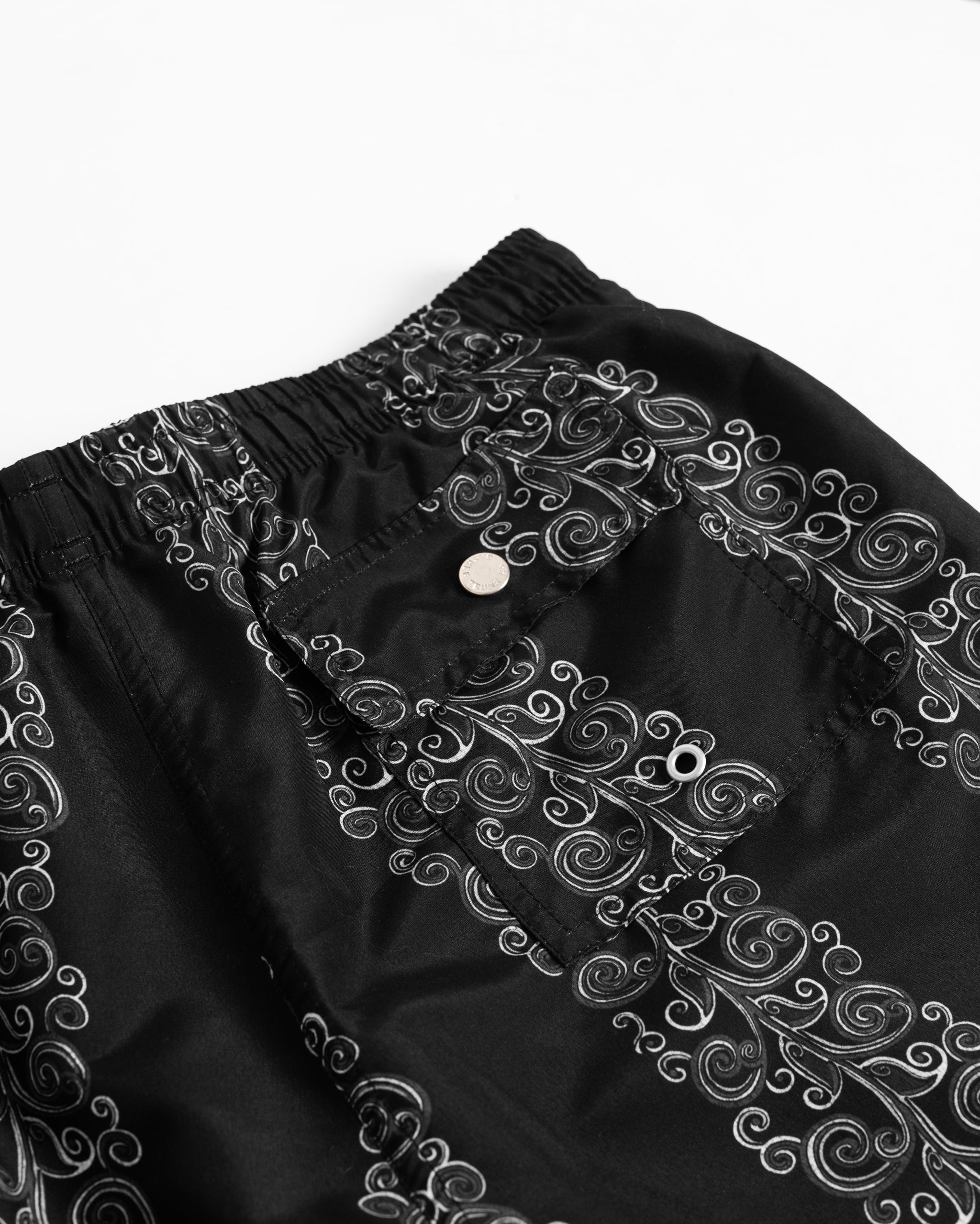 Close-up of men's black swim trunks with grey floral stripe print with button-closure back pocket