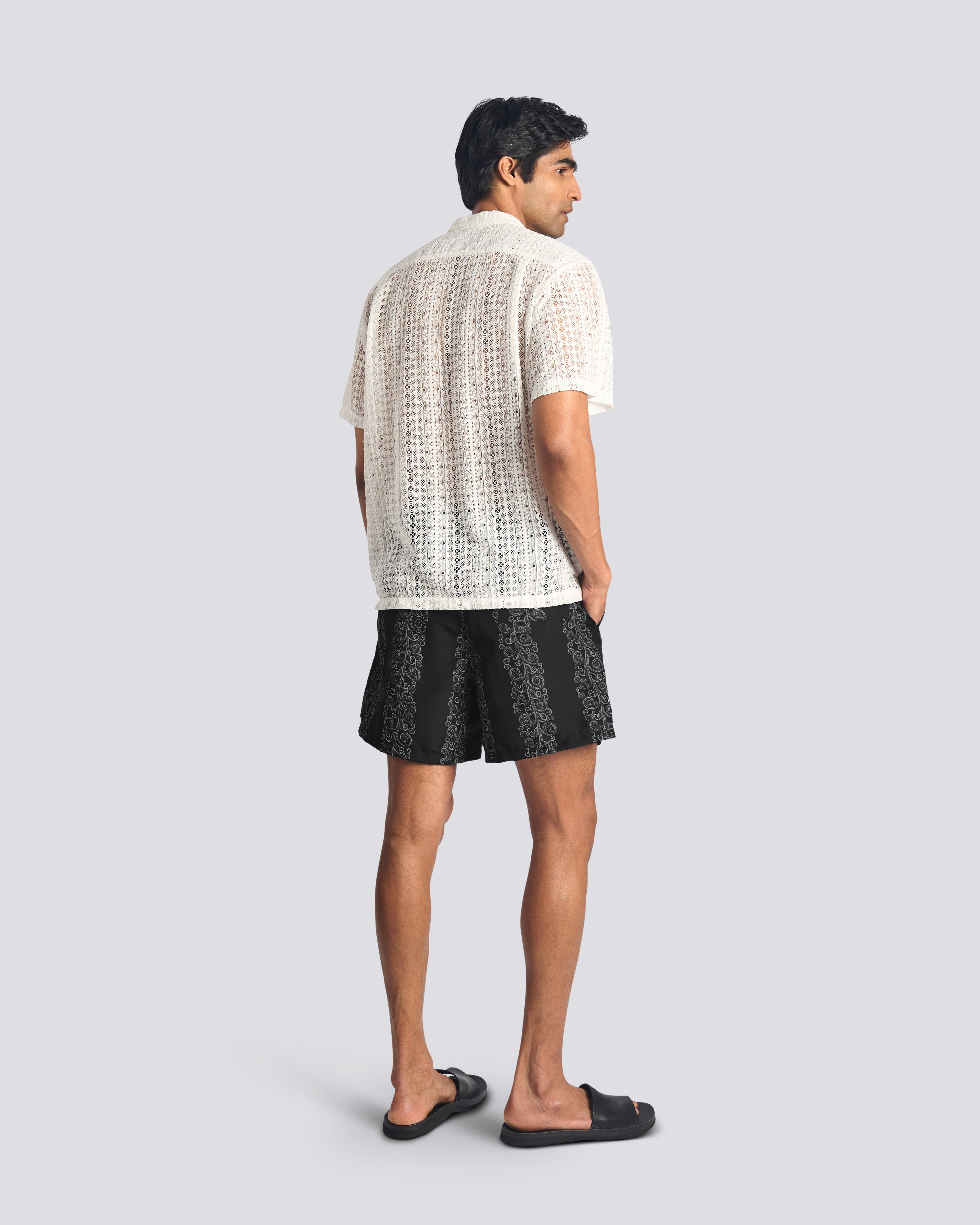 Man wearing black swim trunks with grey floral stripe print with Bather white lace button up short sleeve