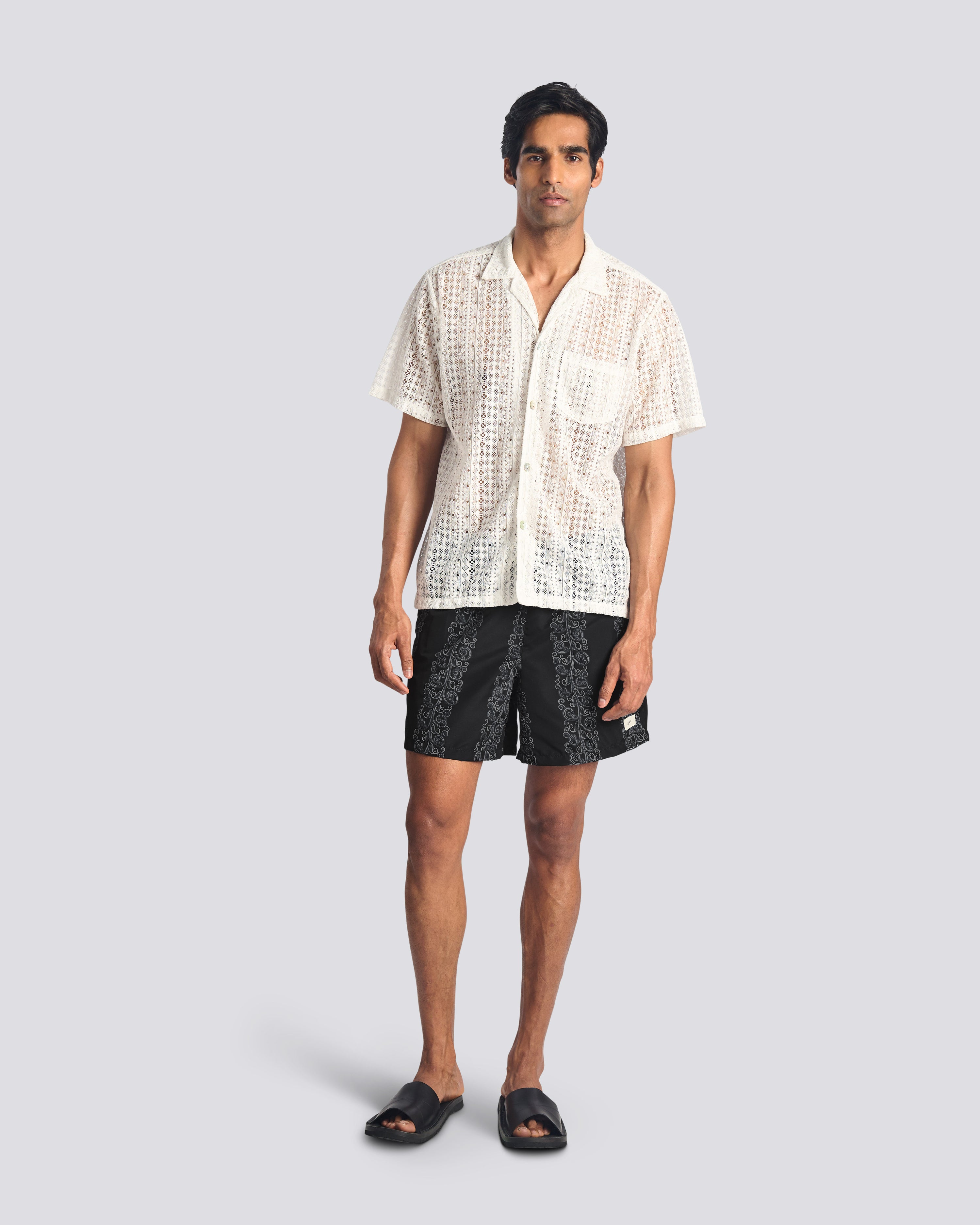 Man wearing black swim trunks with grey floral stripe print with Bather white lace button up short sleeve