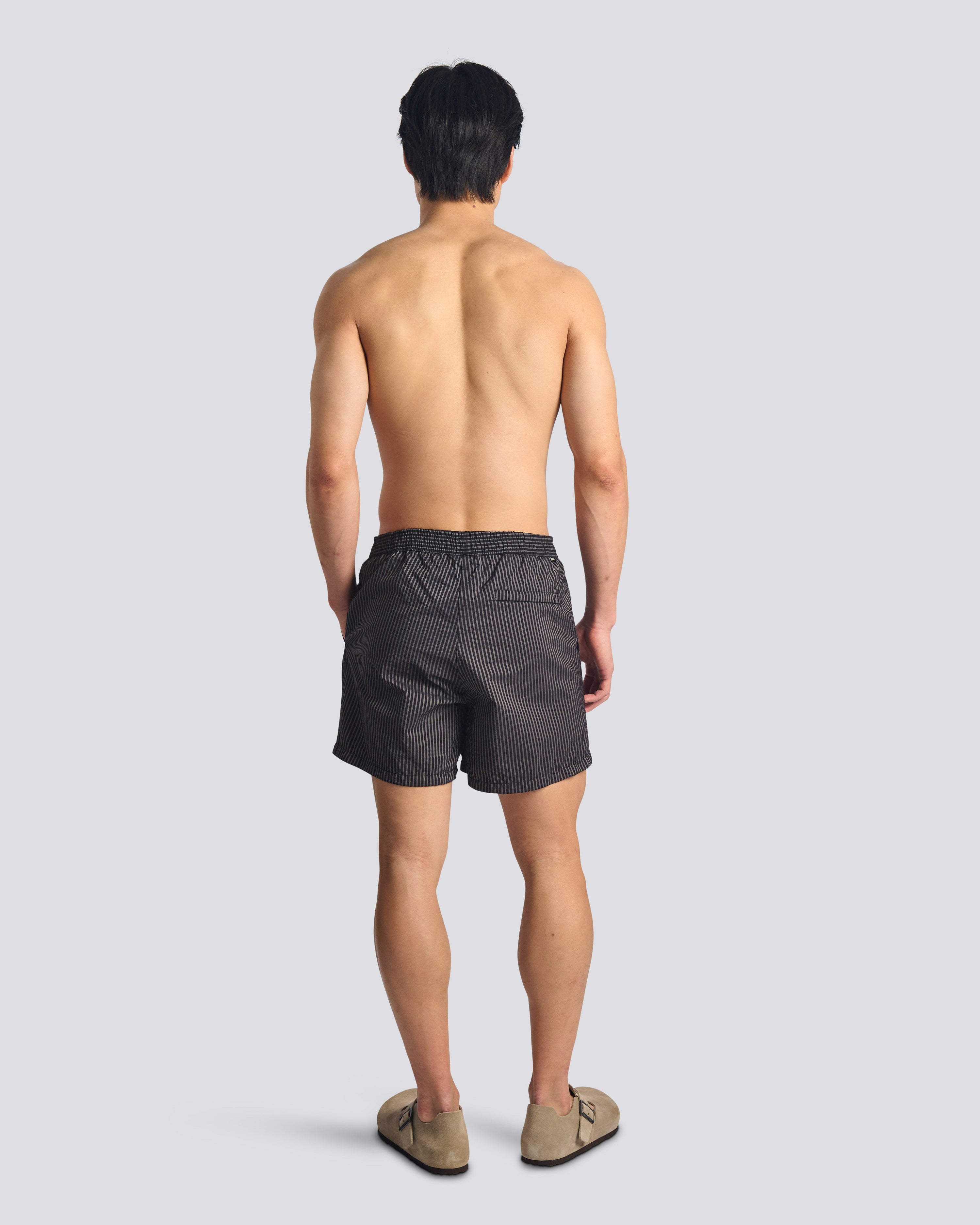 Man wearing men's black pinstripe swim trunks with hidden elastic waistband