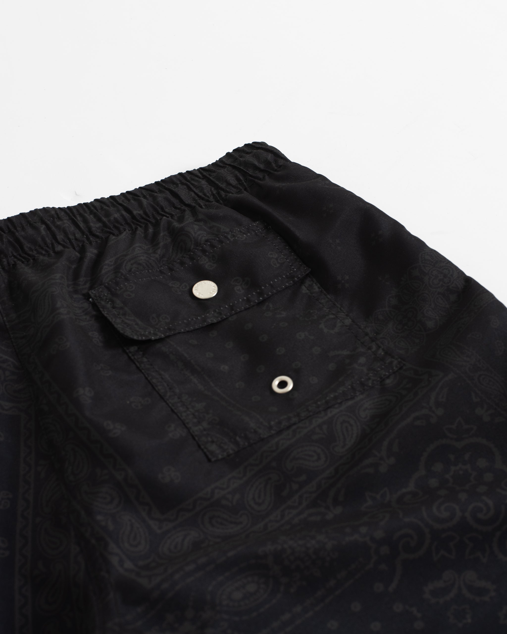 Close-up of the back button-closure pocket on men’s black swim trunks with bandana pattern