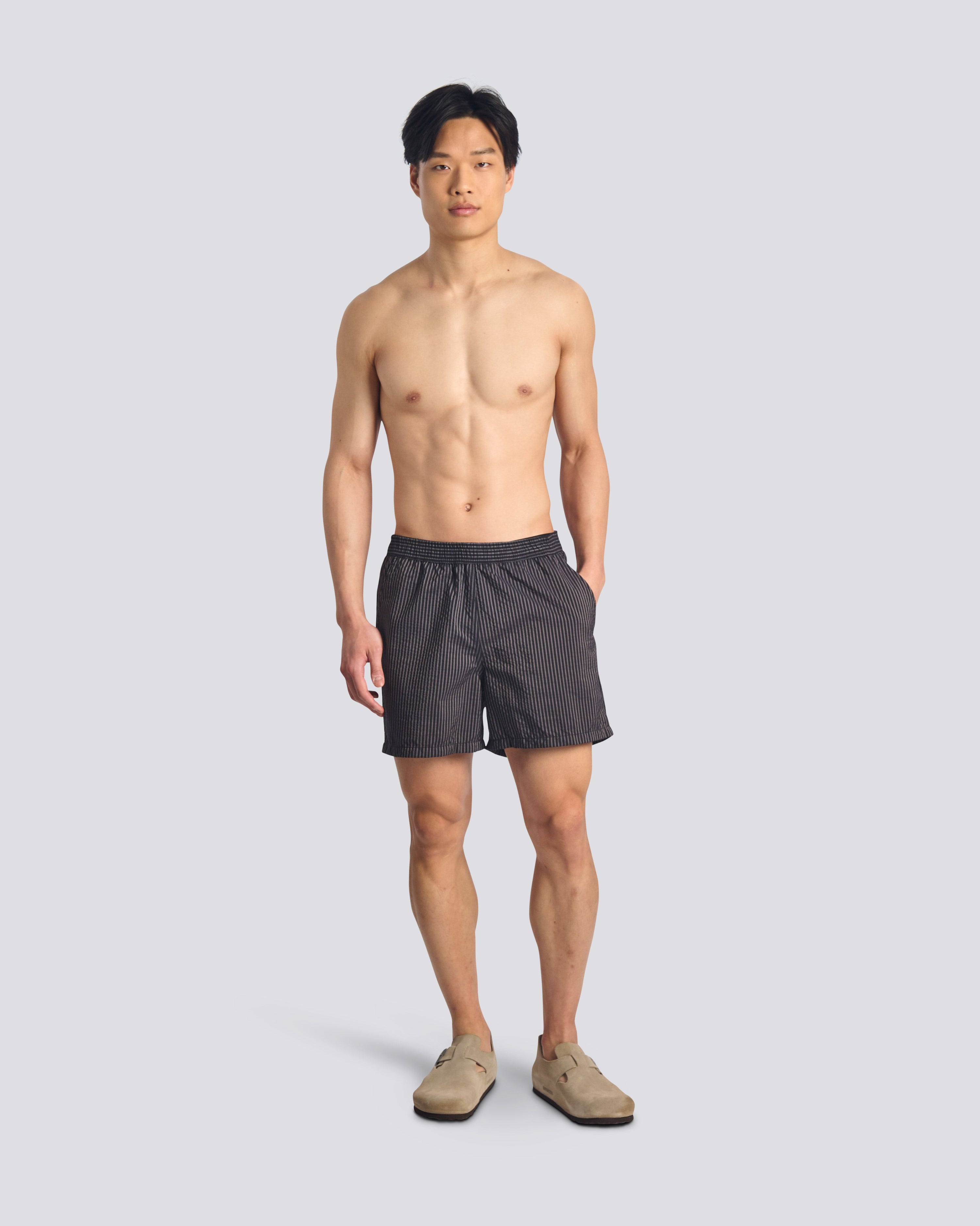 Man wearing men's black pinstripe swim trunks with hidden elastic waistband