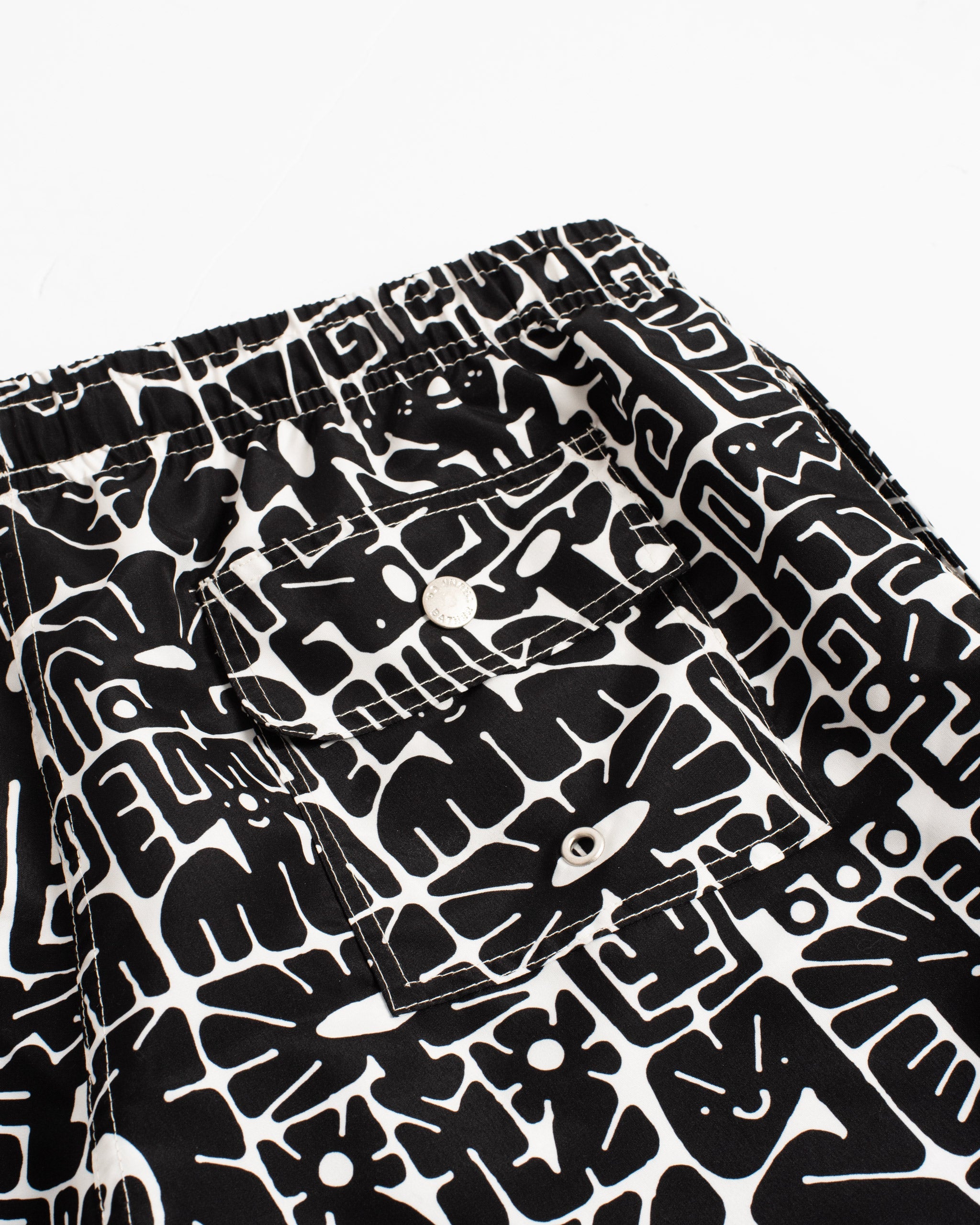 Close-up of the back button-closure pocket on men’s black and white geometric-print swim trunks