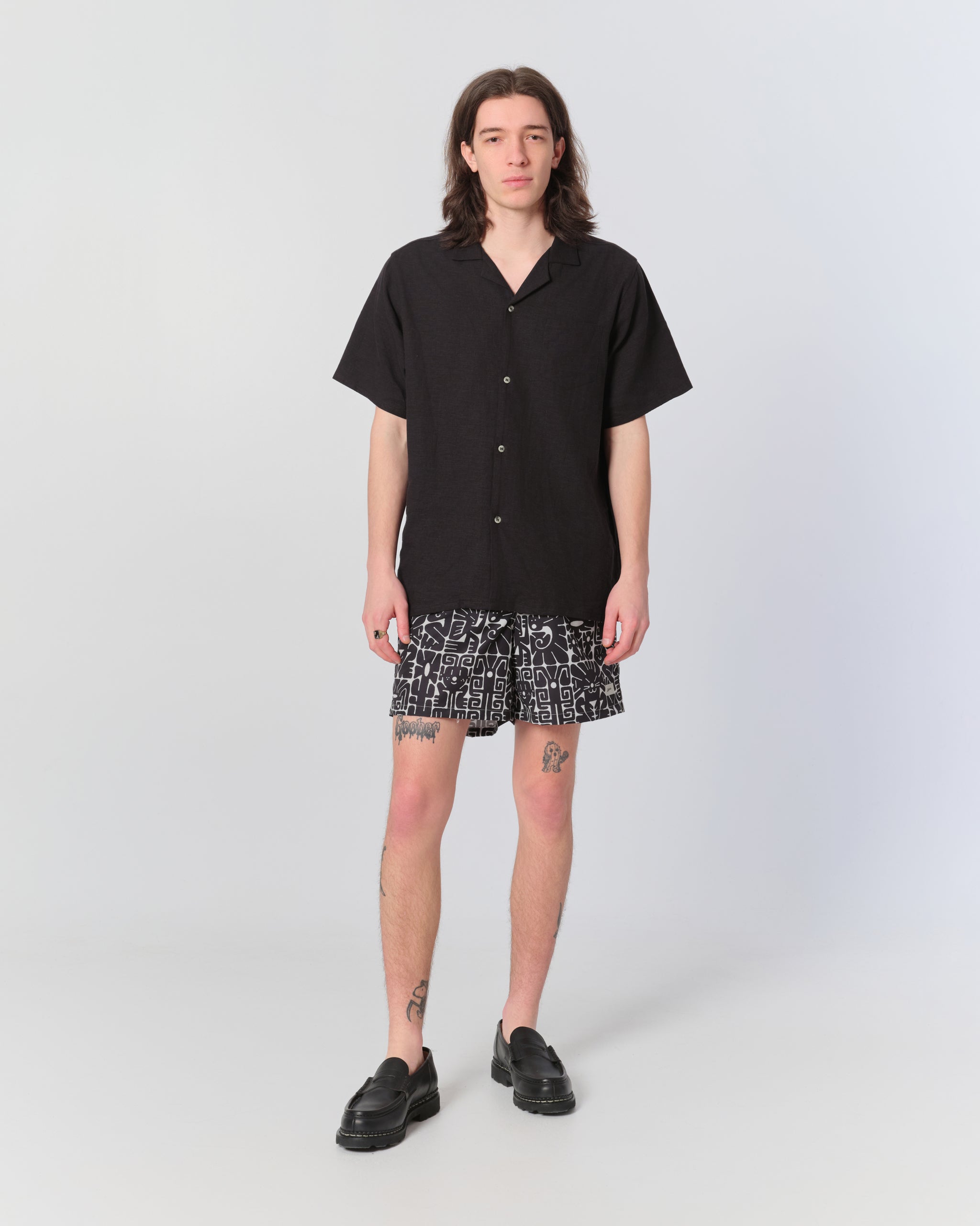 Male model wearing black and white geometric-print swim trunks with a Bather black short-sleeve camp shirt