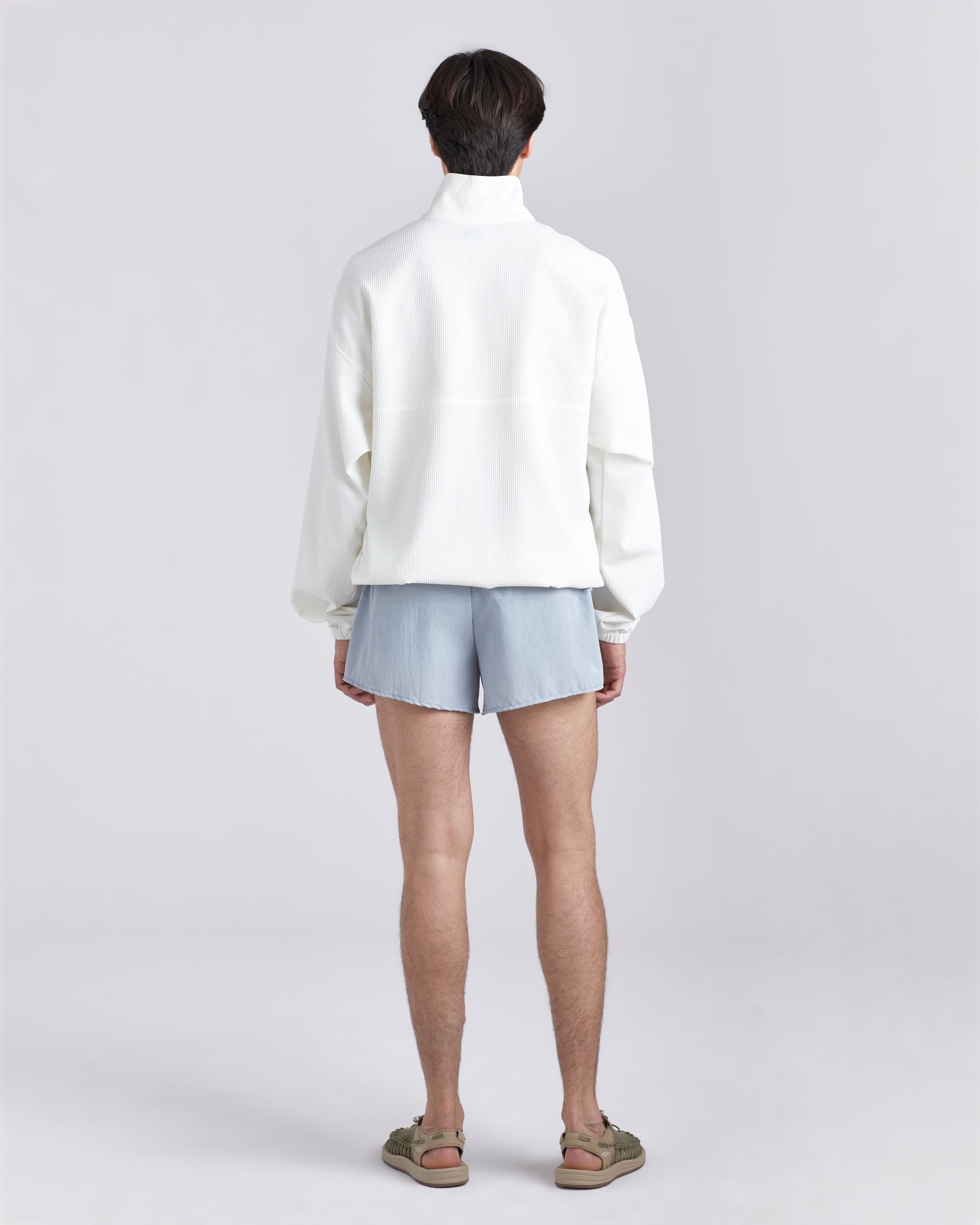 Back view of model wearing white wind breaker and 3.5 inch inseam Bather Active Trunk in blue featuring lightweight recycled Japanese DotAir nylon with stretch fabric and compression liner