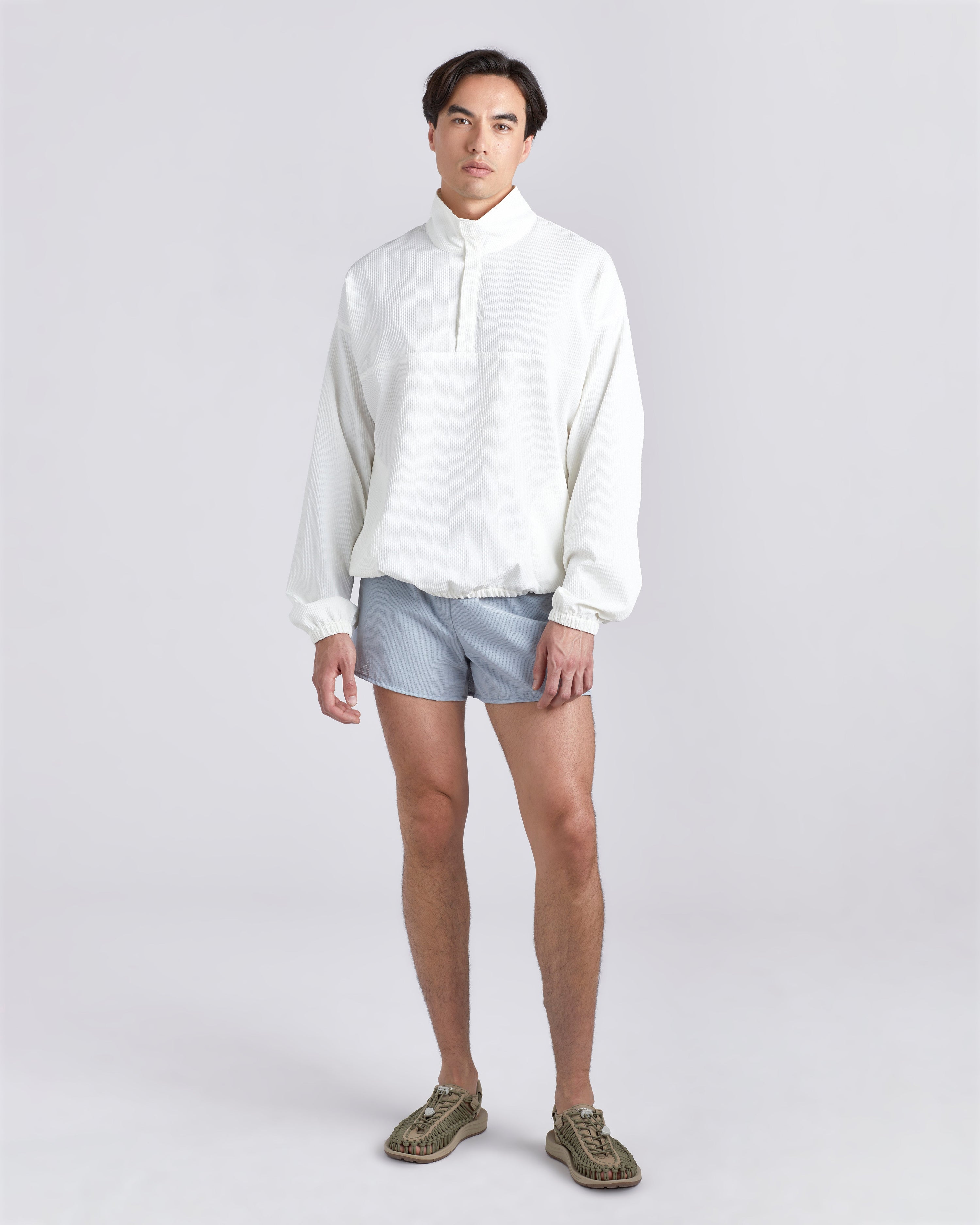 Front view of model wearing white wind breaker and 3.5 inch inseam Bather Active Trunk in blue featuring lightweight recycled Japanese DotAir nylon with stretch fabric and compression liner