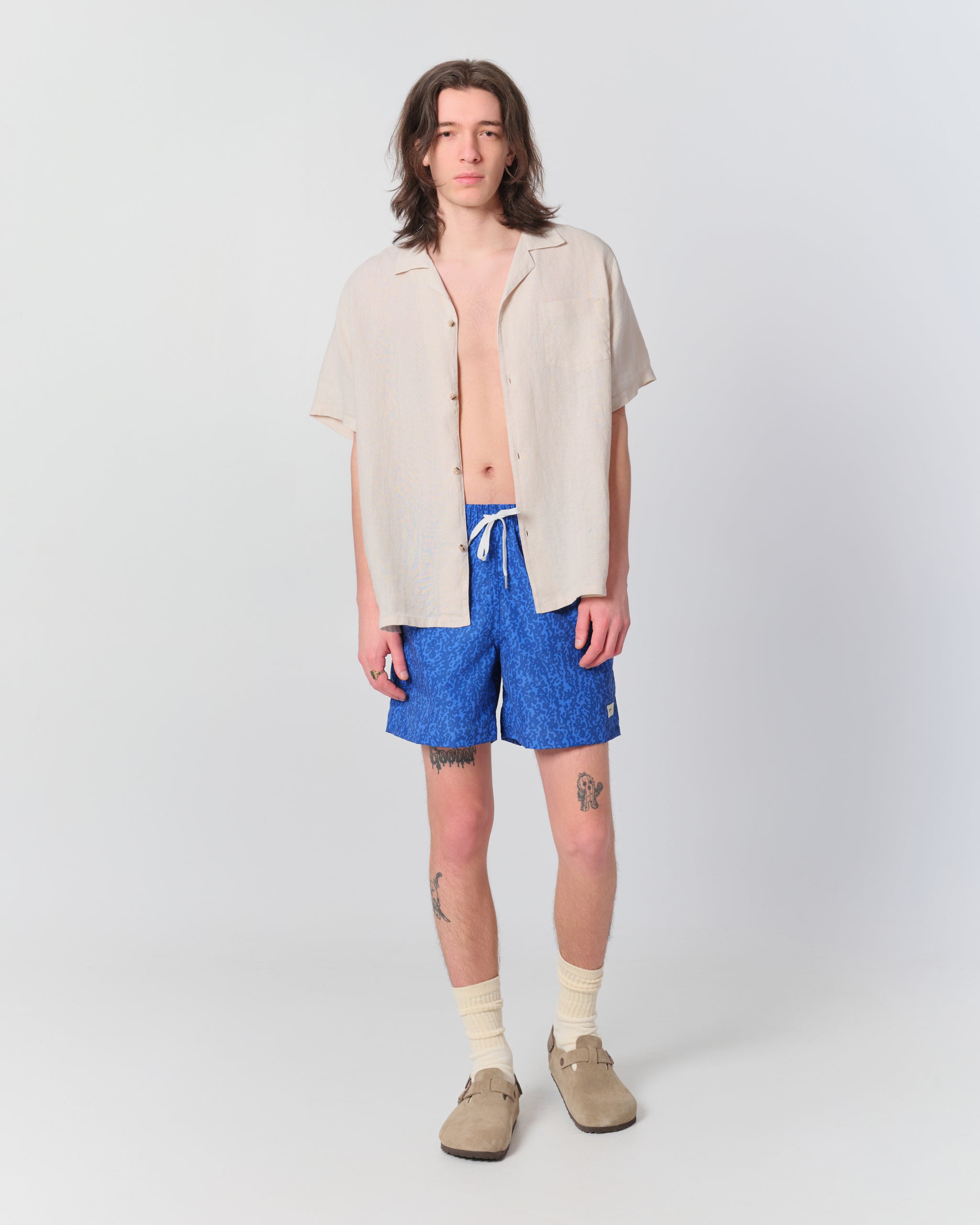 Male model wearing a white camp shirt and blue swim trunks with a camo pattern