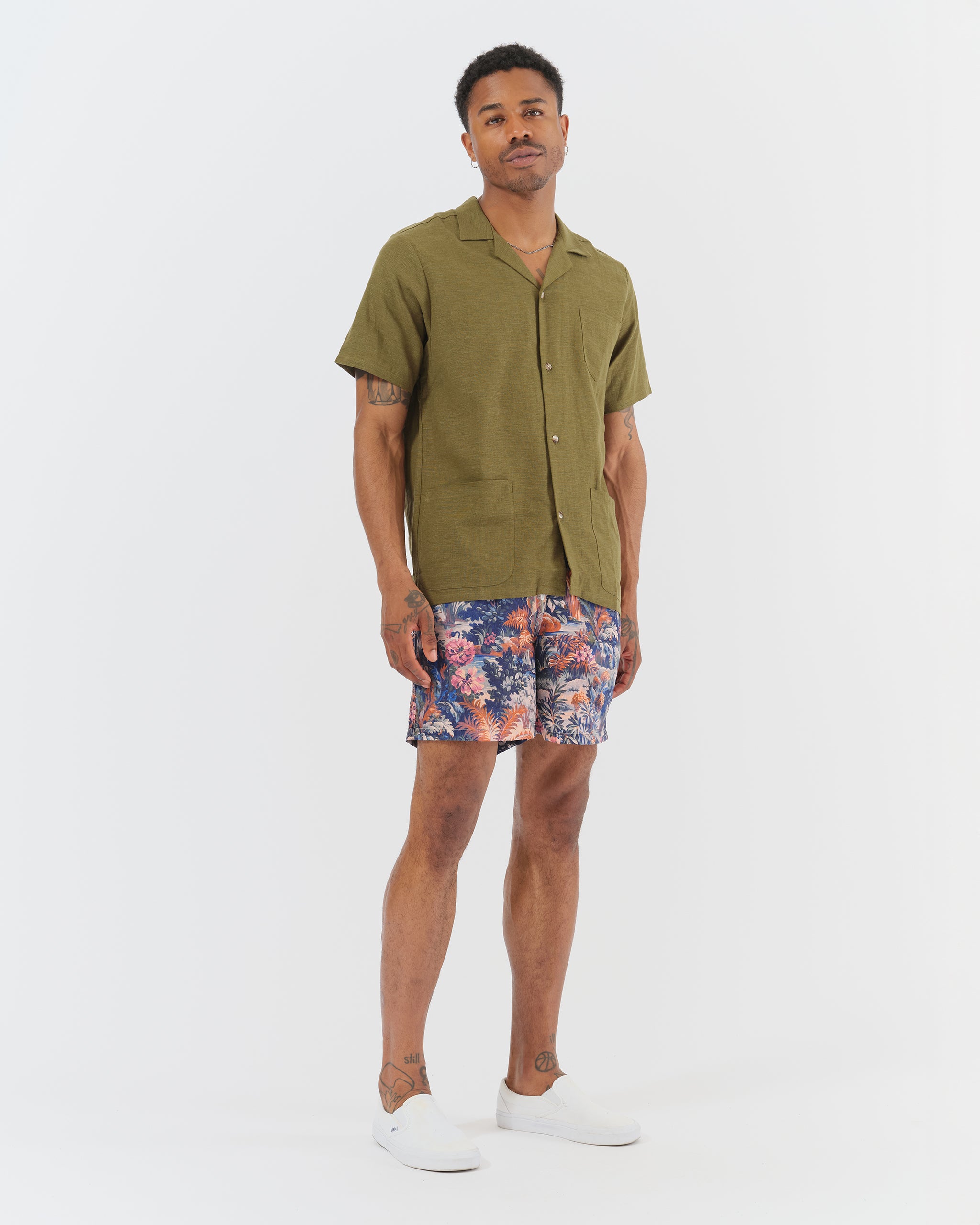 Male model wearing tropical floral swim trunks with an olive green short-sleeve camp shirt