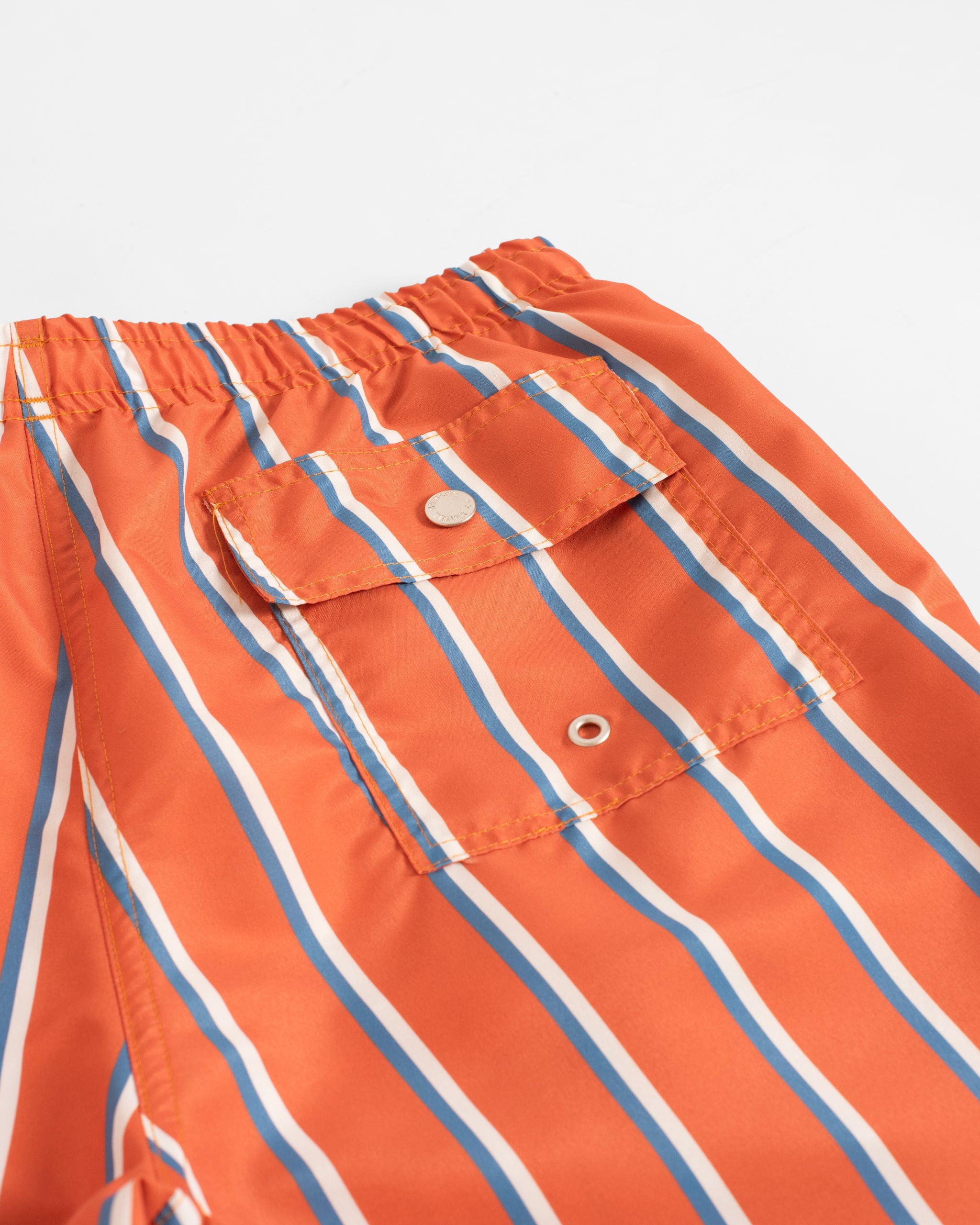 Close-up of the back button-closure pocket on men’s orange swim trunks with blue and white vertical stripe pattern