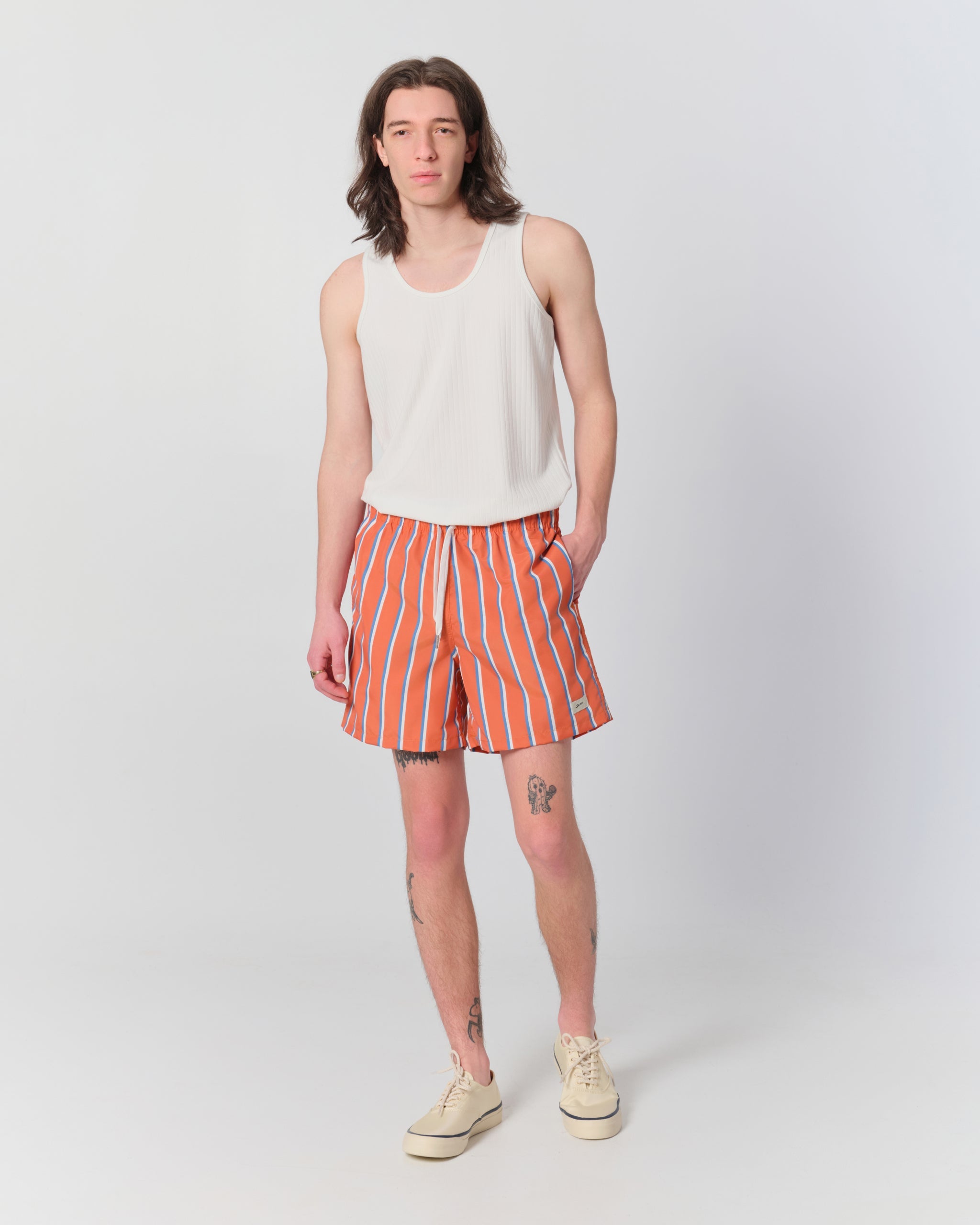 Male model wearing orange swim trunks with blue and white vertical stripe pattern and drawstring waistband