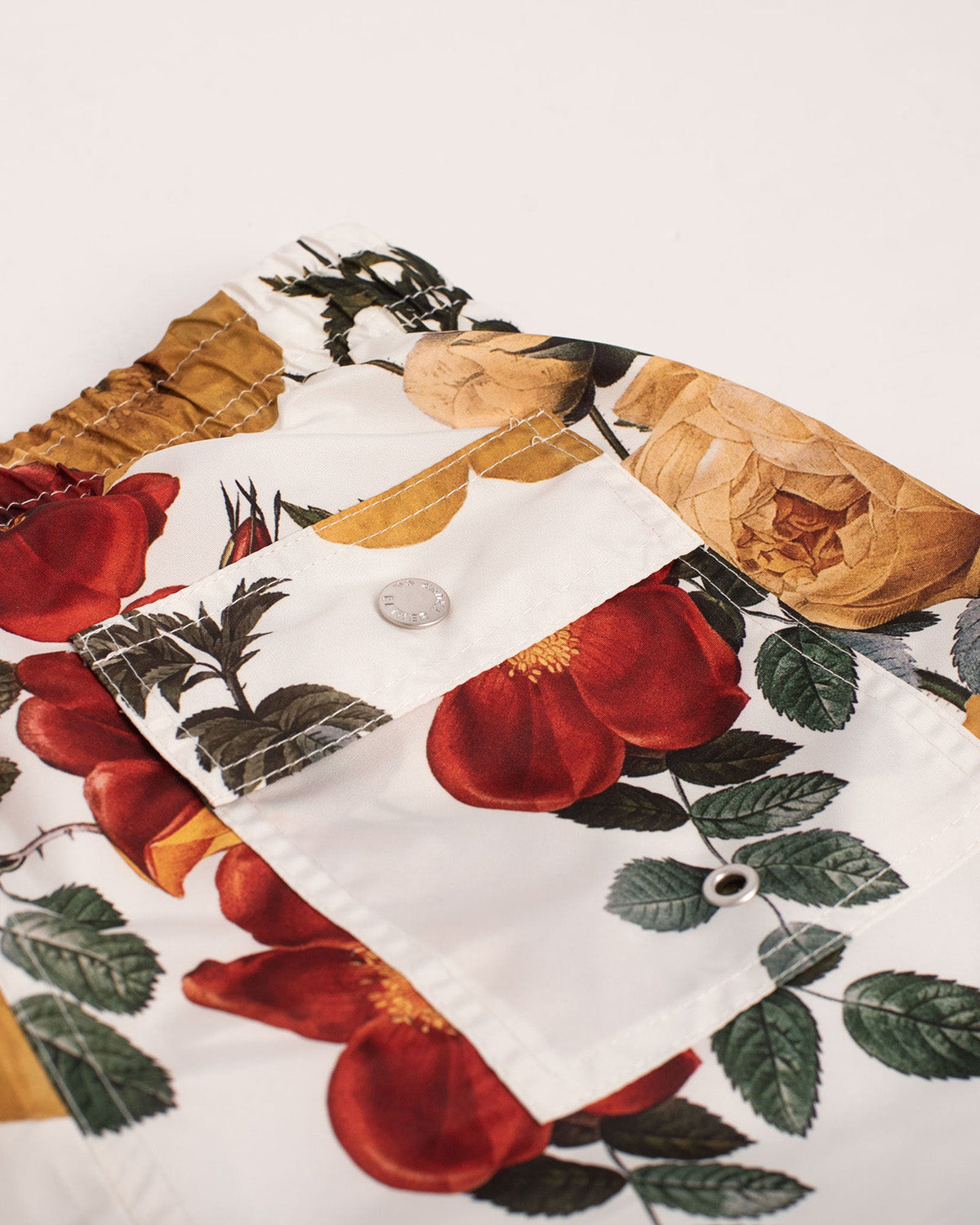 Close up of ivory swim trunks with vintage floral print and button closure pocket 