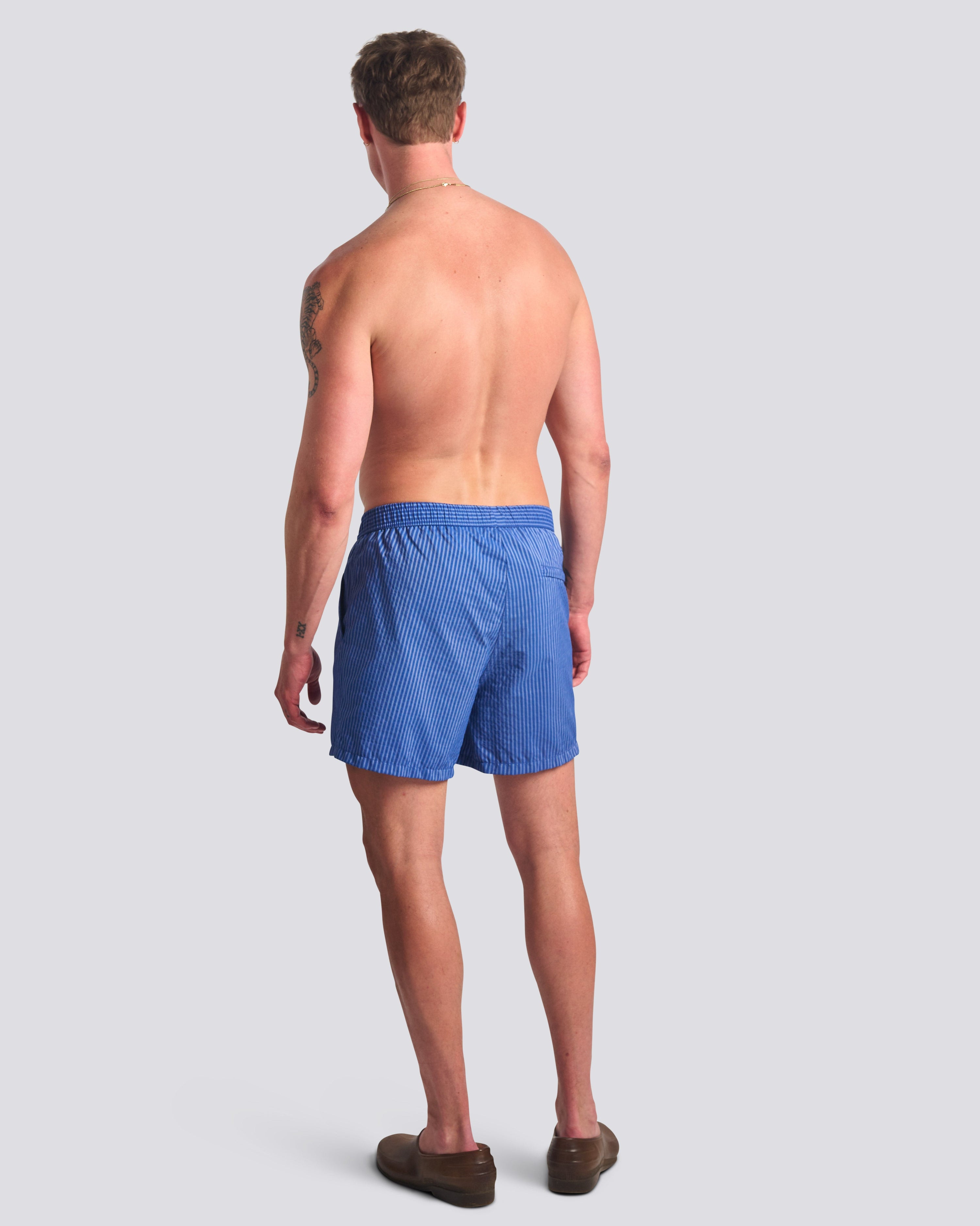 Man wearing men's blue pinstripe swim trunks with hidden elastic waistband