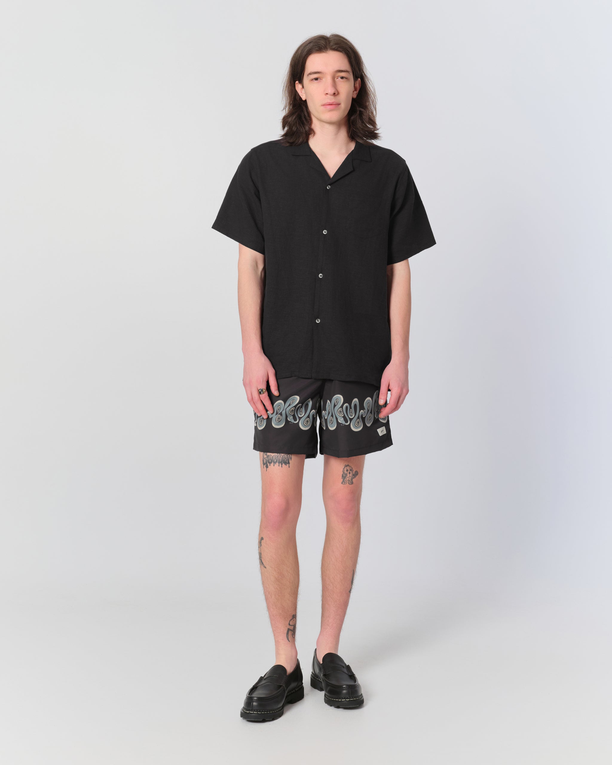 Male model wearing men's black swim trunk with graphic snake border pattern 