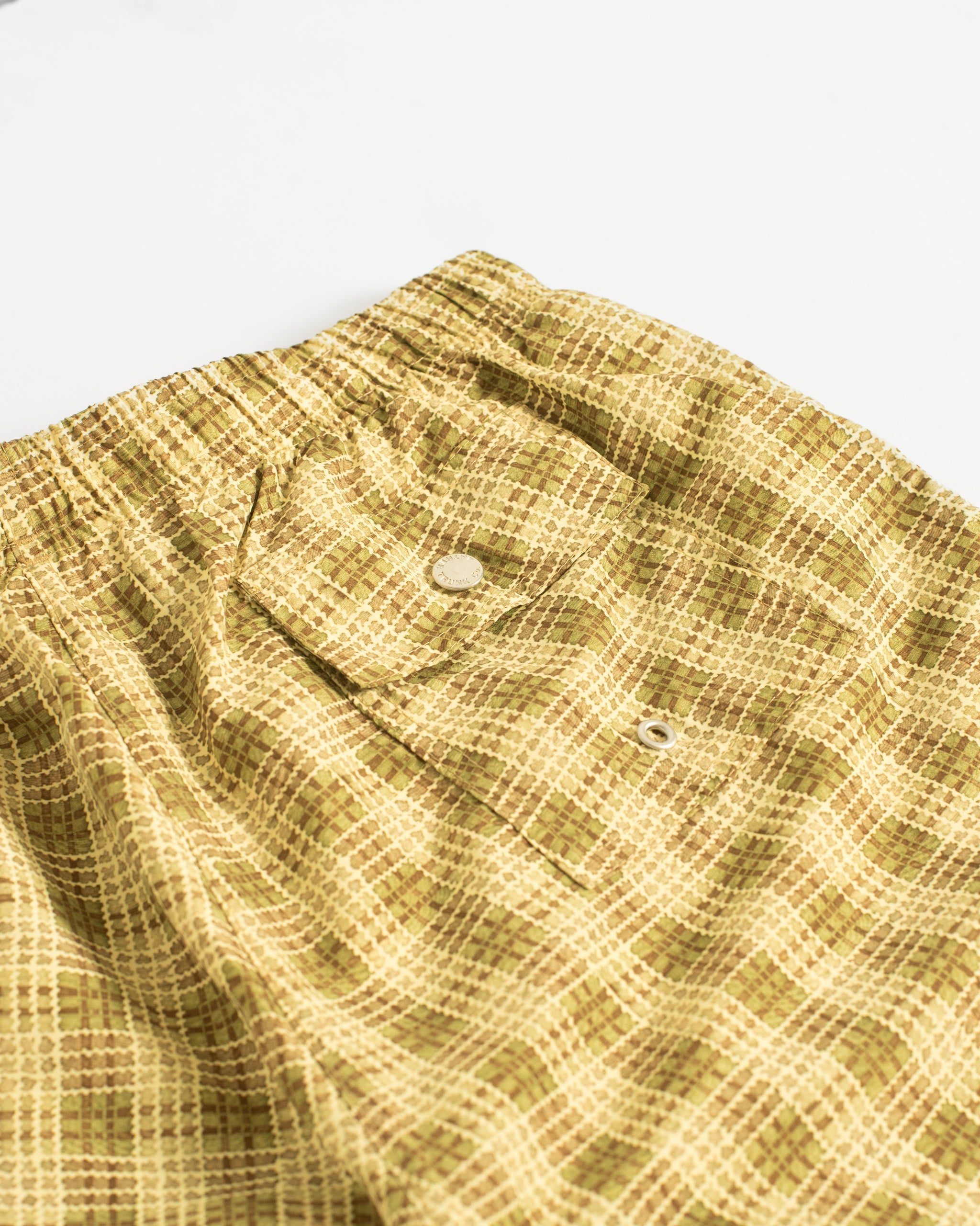 Close up of men’s yellow plaid patterned swim trunks with button closure back pocket 
