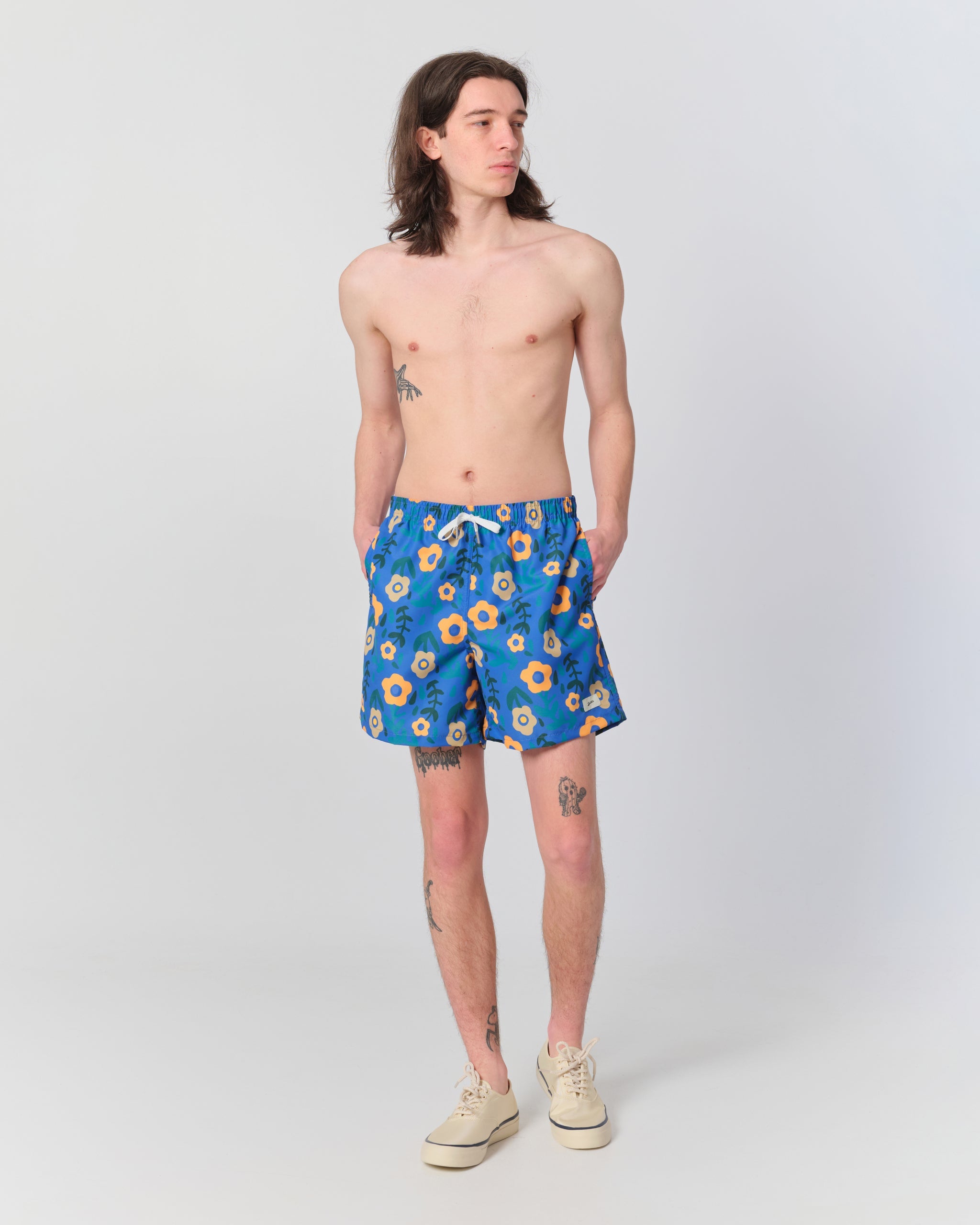 Male model wearing men’s blue floral swim trunks with orange flower print and elastic drawstring waistband