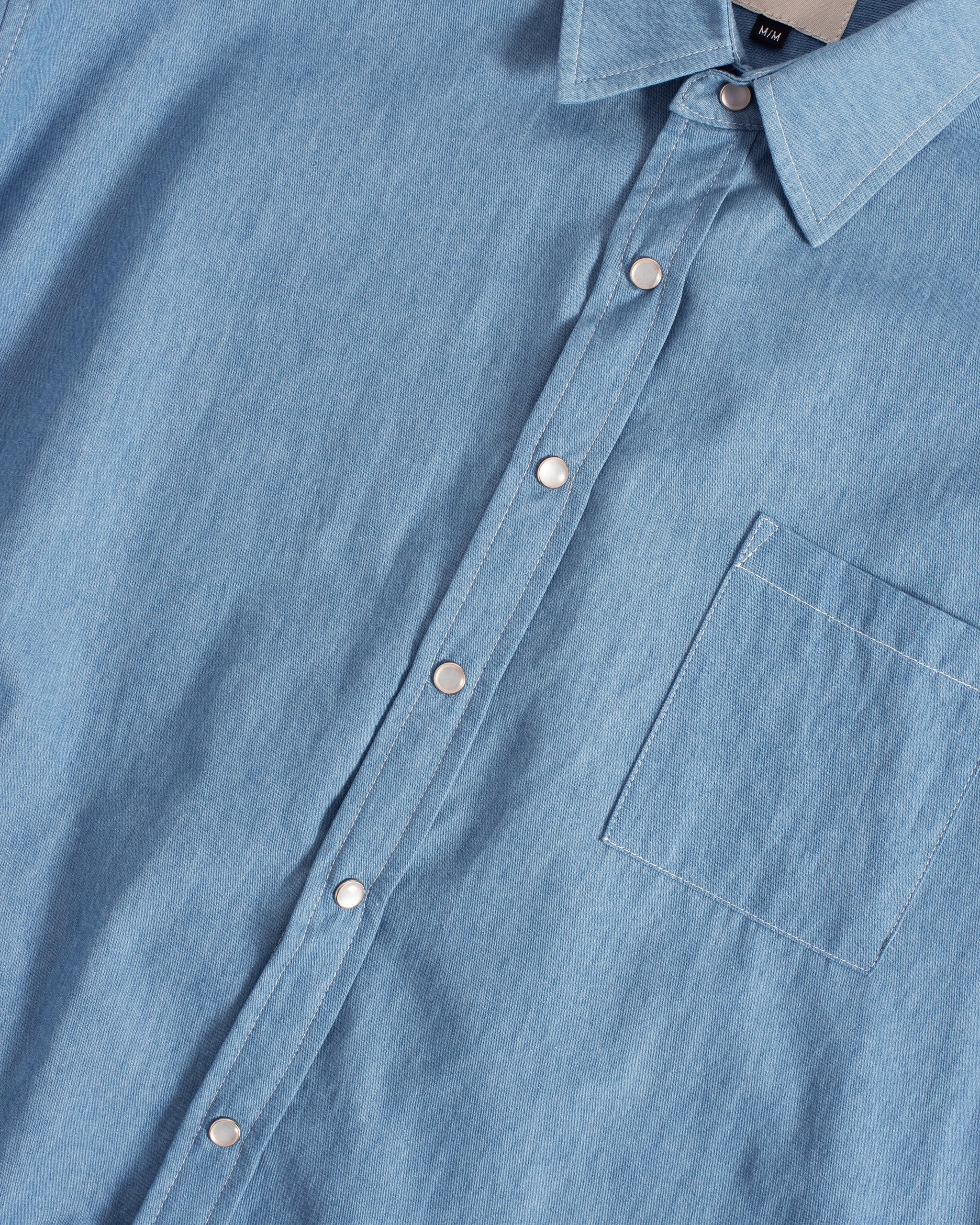 Detailed view of the fabric, pocket, and snap buttons on the Bather Men's light blue denim shirt.