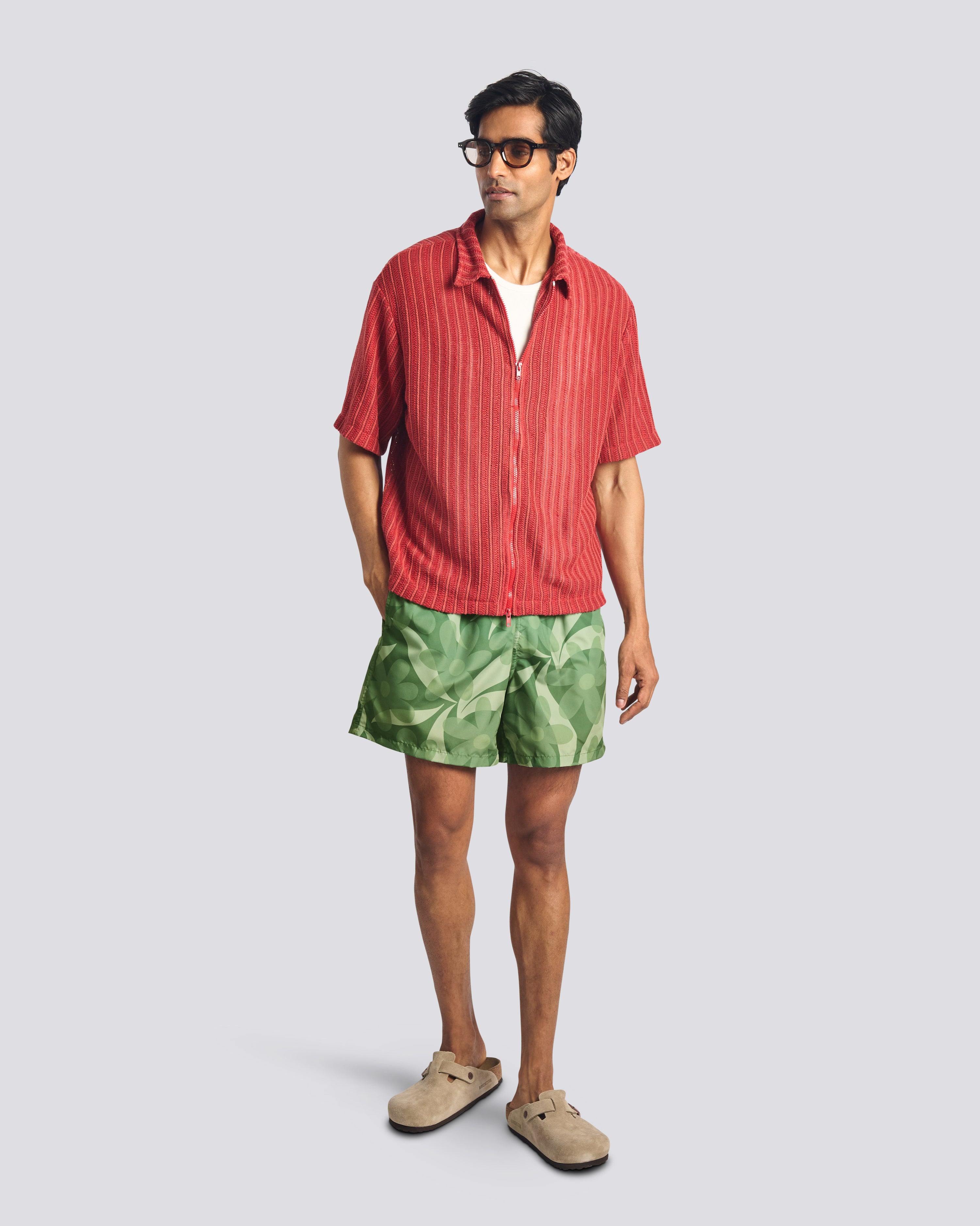 Man wearing green floral swim trunks with Bather red short sleeve shirt