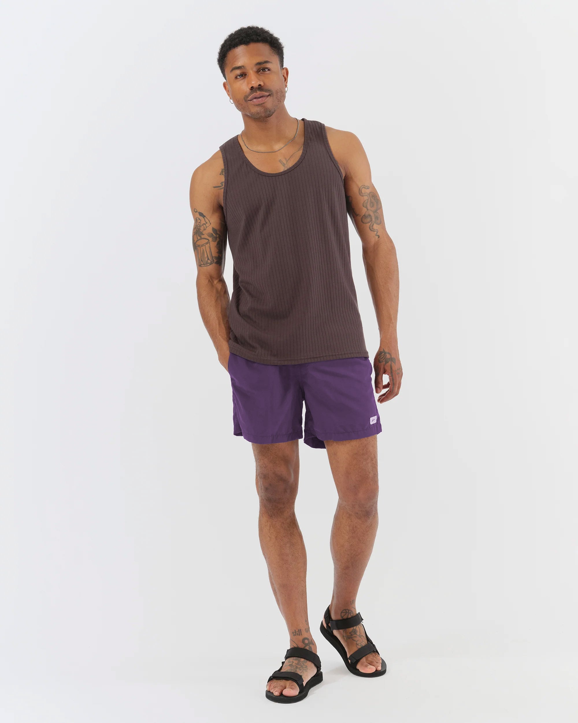 Man wearing a brown tank top and purple shorts on a white background