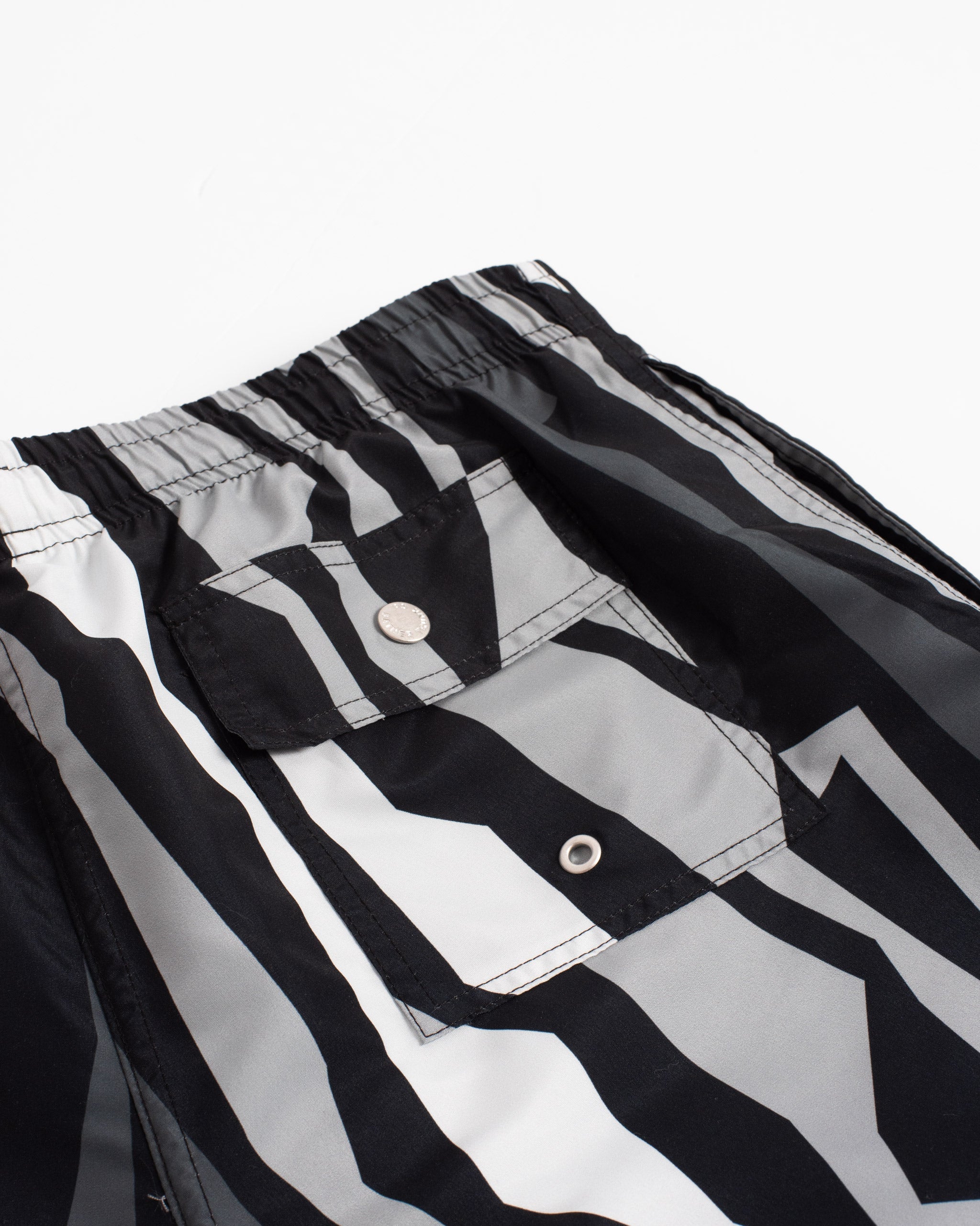 Close-up of men’s of black and gray swim trunks in vertical jagged geometric striped pattern with button closure back pocket