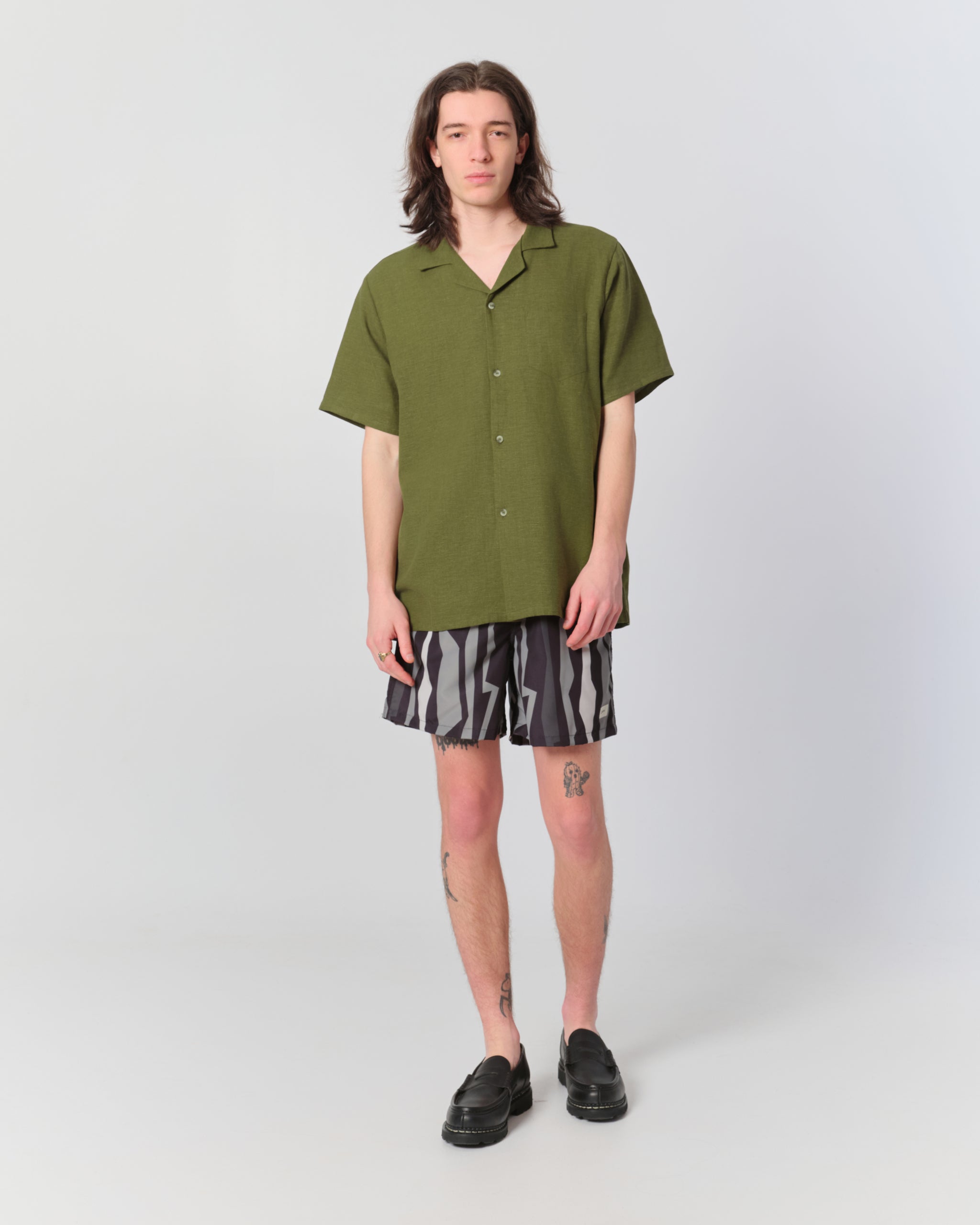Male model wearing black and gray swim trunks with vertical jagged geometric striped pattern and olive camp shirt