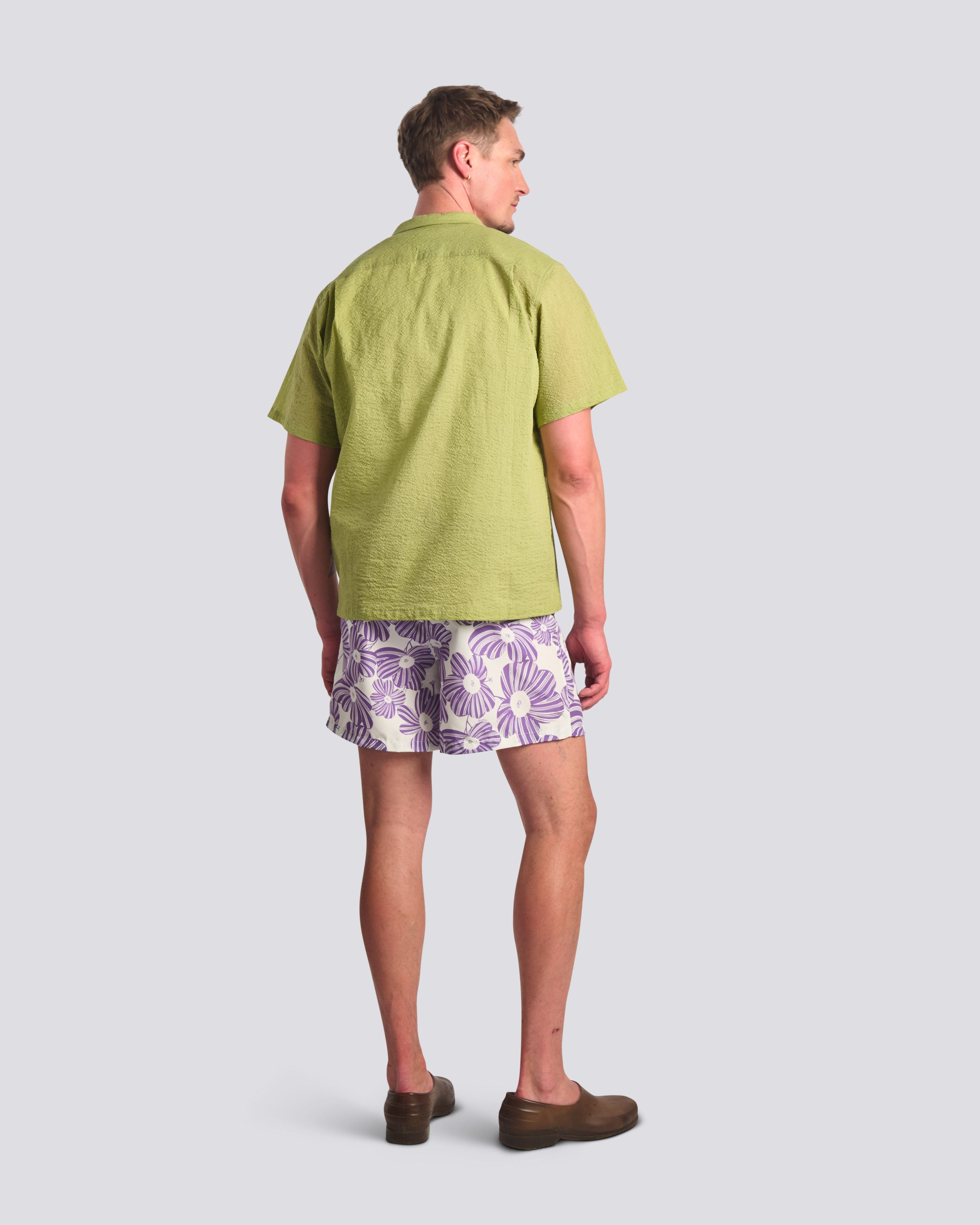 Person wearing a green shirt and patterned shorts on a light gray background