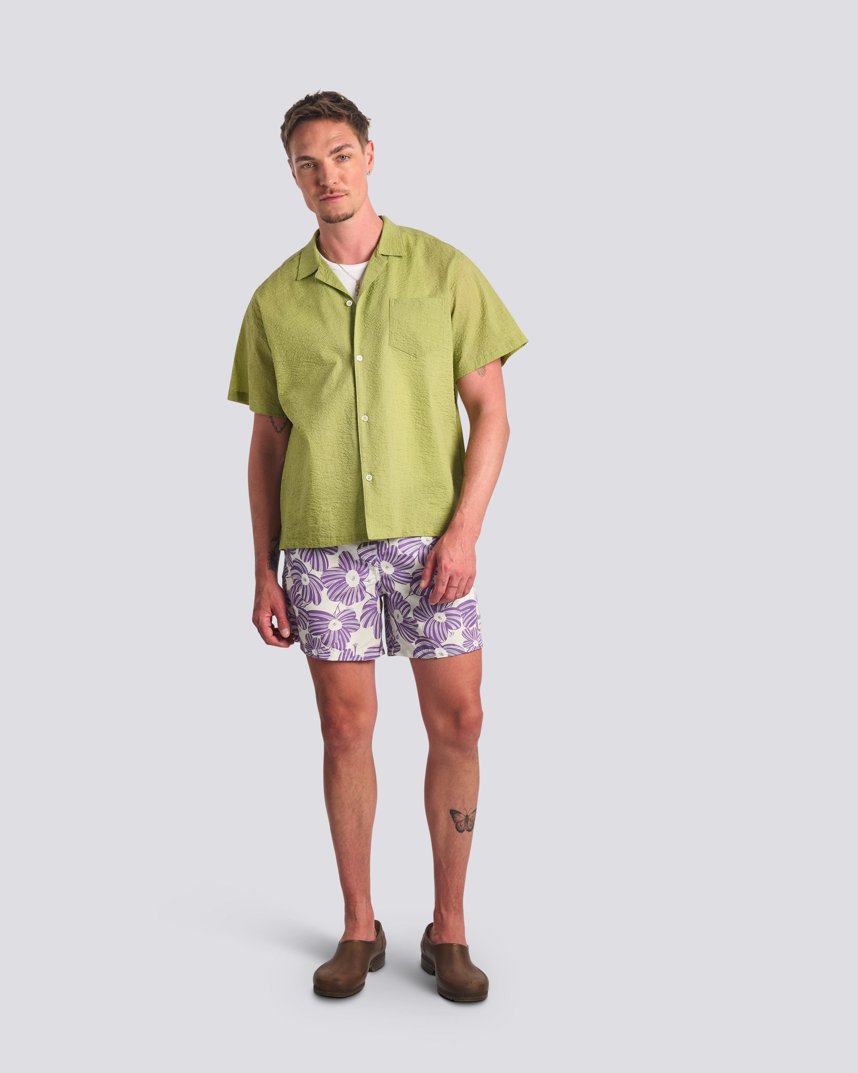 Man wearing a green shirt and patterned shorts on a light gray background