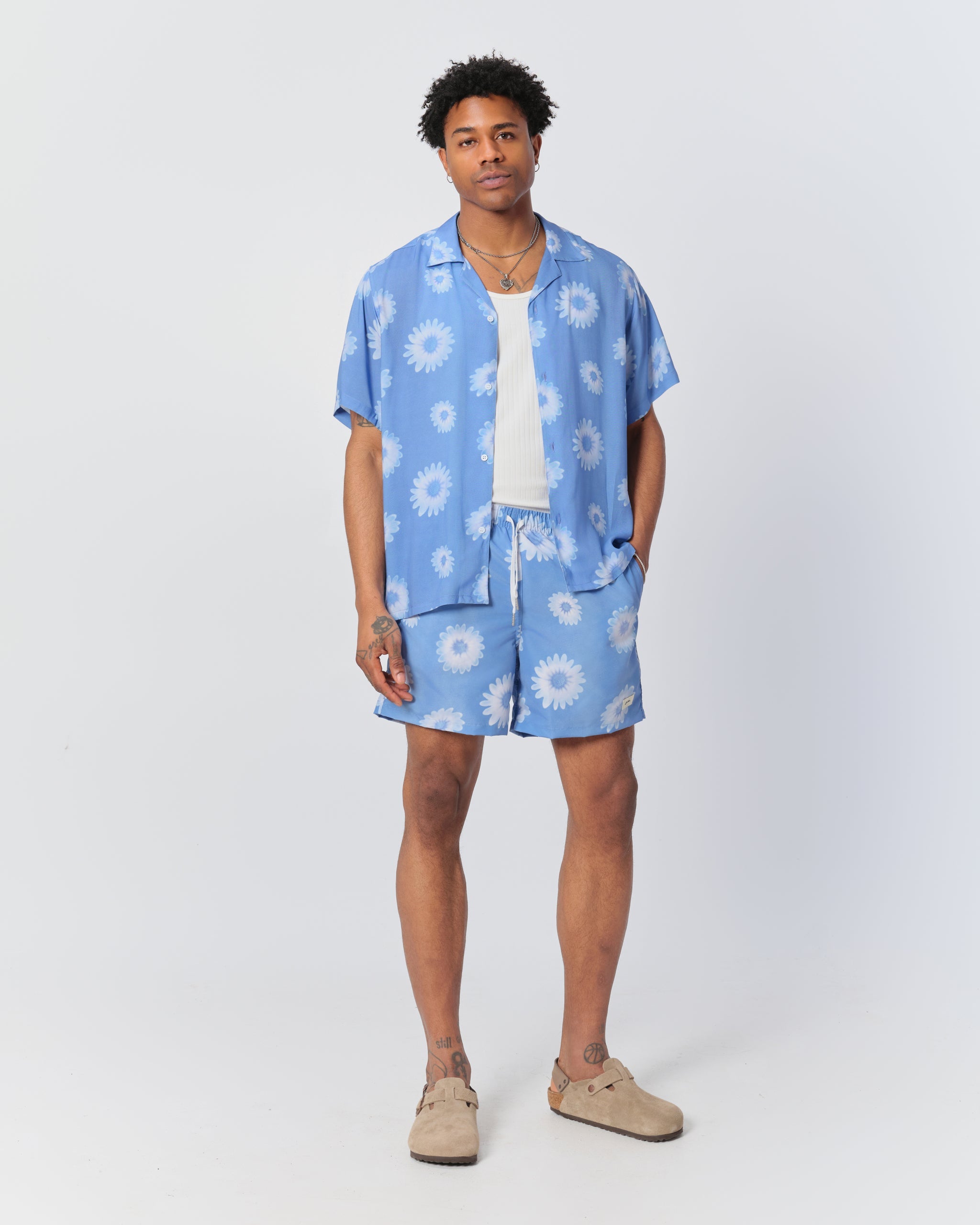 Man wearing all over print swim trunks with white daisy pattern in light blue and matching Bather white daisy pattern camp shirt