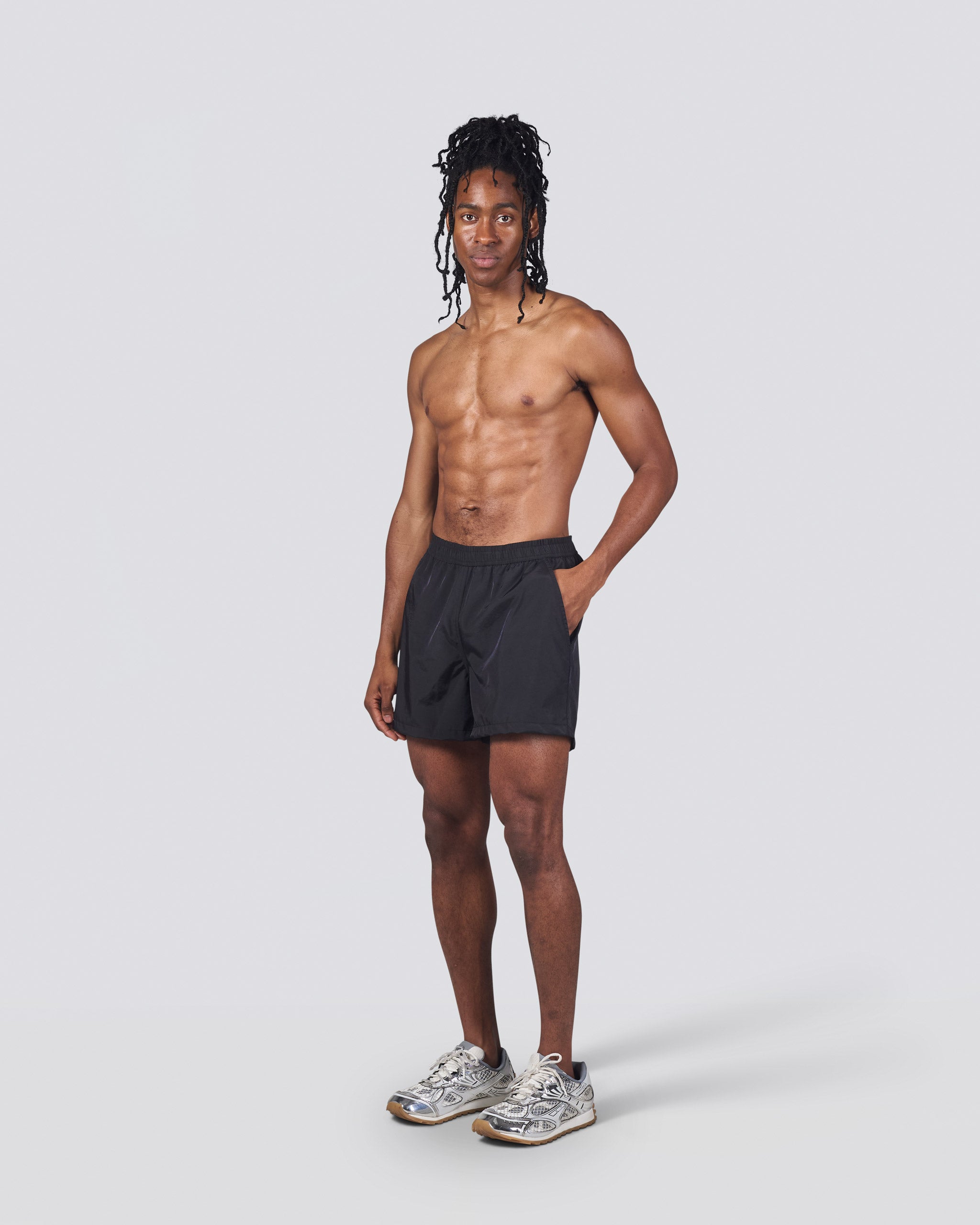 Shirtless man wearing shiny black swim trunk featuring an elastic drawstring waistband on white background