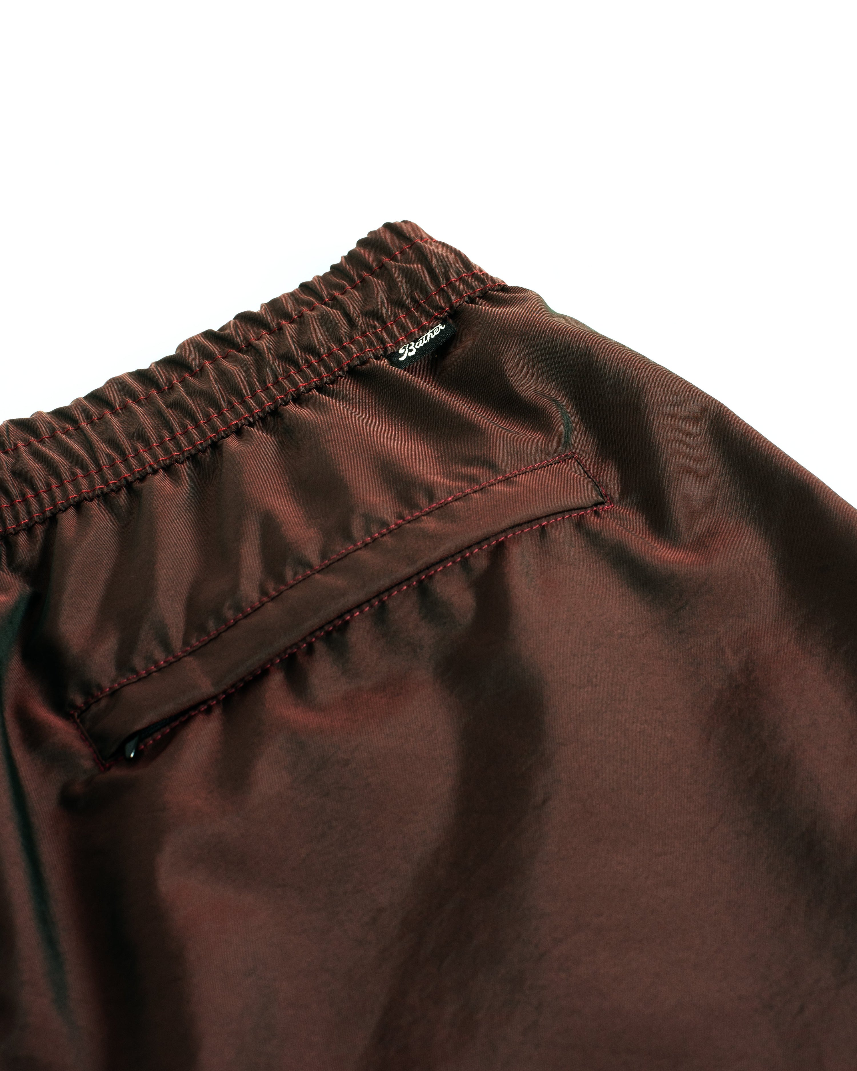 Detail close up view of men's shiny swim trunk in brown featuring zipper closure back pocket on white background