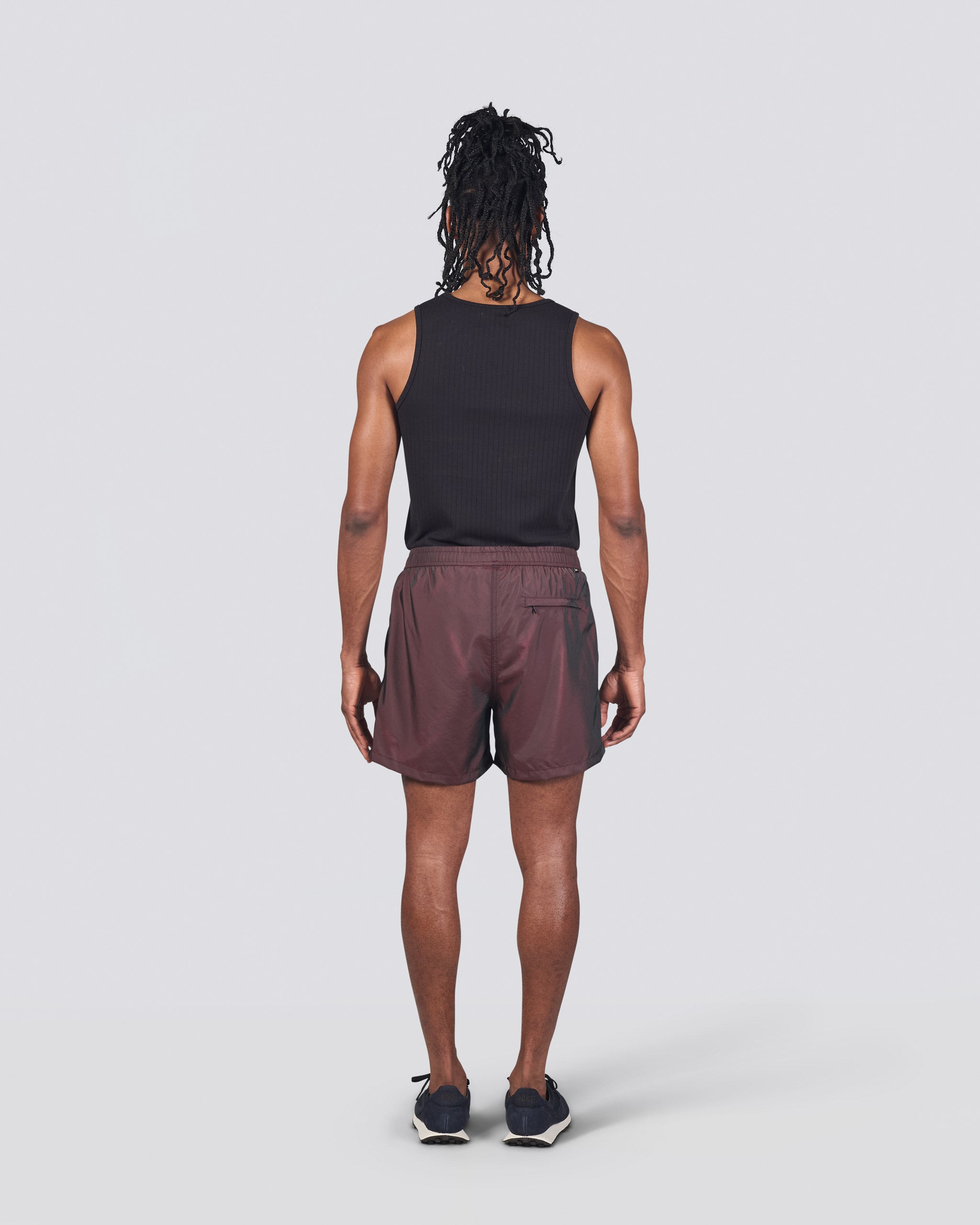 Back of man in black tank top wearing shiny brown swim trunk featuring an elastic drawstring waistband on white background