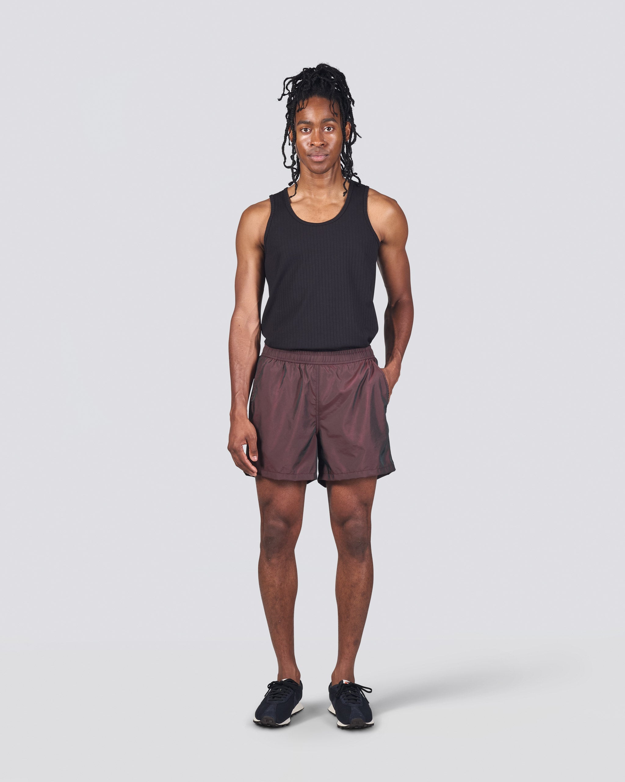 Man in black tank top wearing shiny brown swim trunk featuring an elastic drawstring waistband on white background