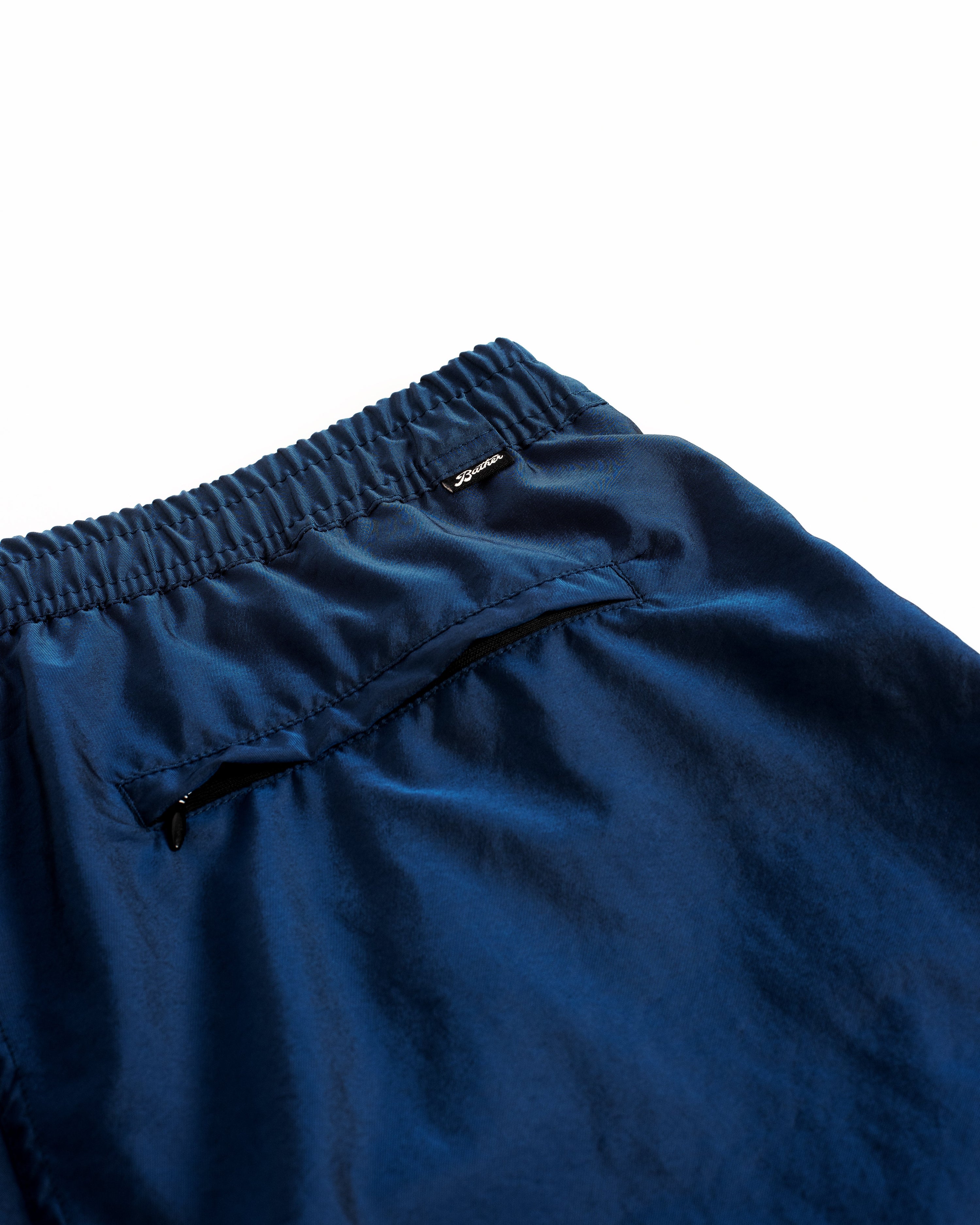 Detail close up view of men's shiny swim trunk in dark blue featuring zipper closure back pocket on white background