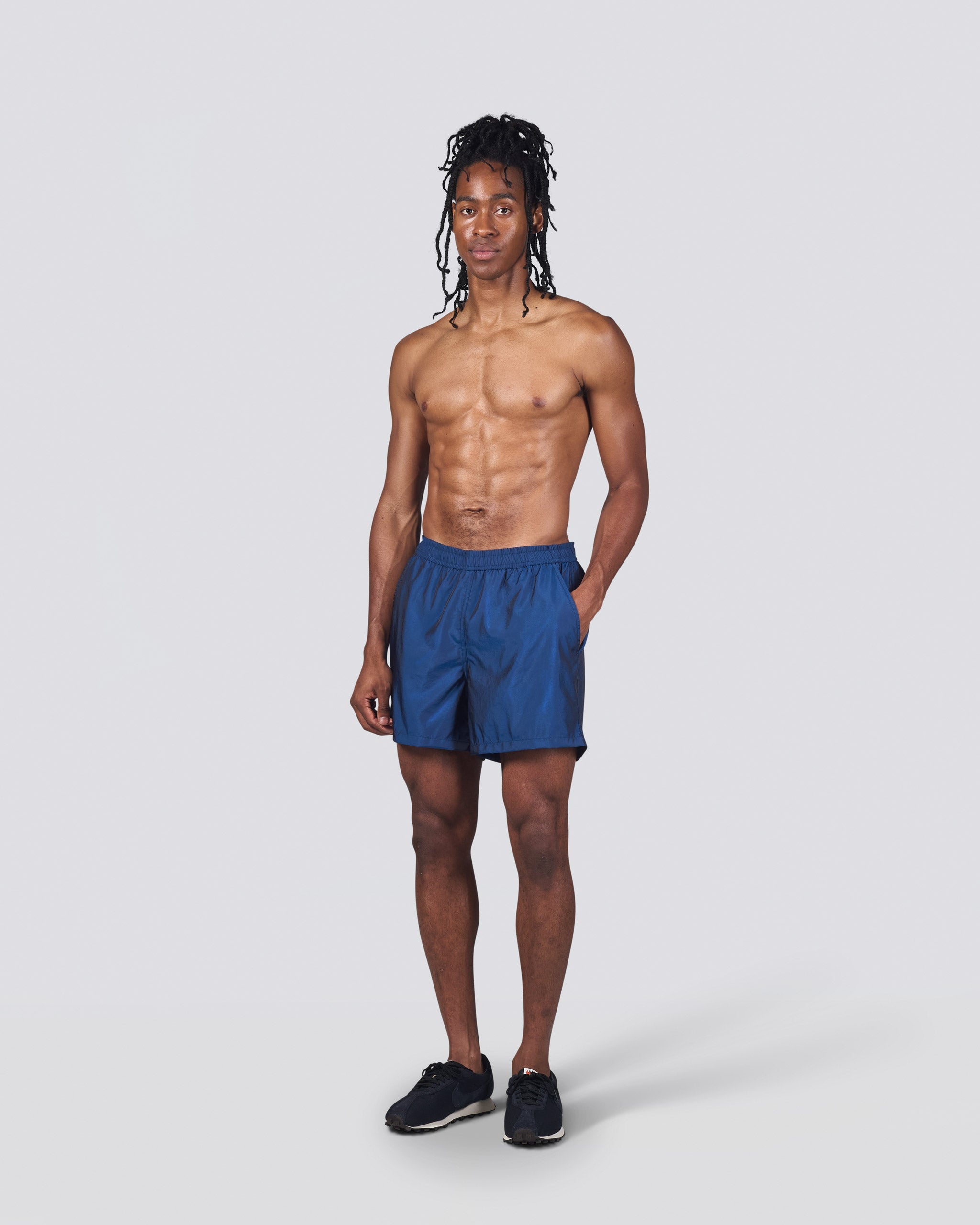 Shirtless man wearing shiny dark blue swim trunk featuring an elastic drawstring waistband on white background