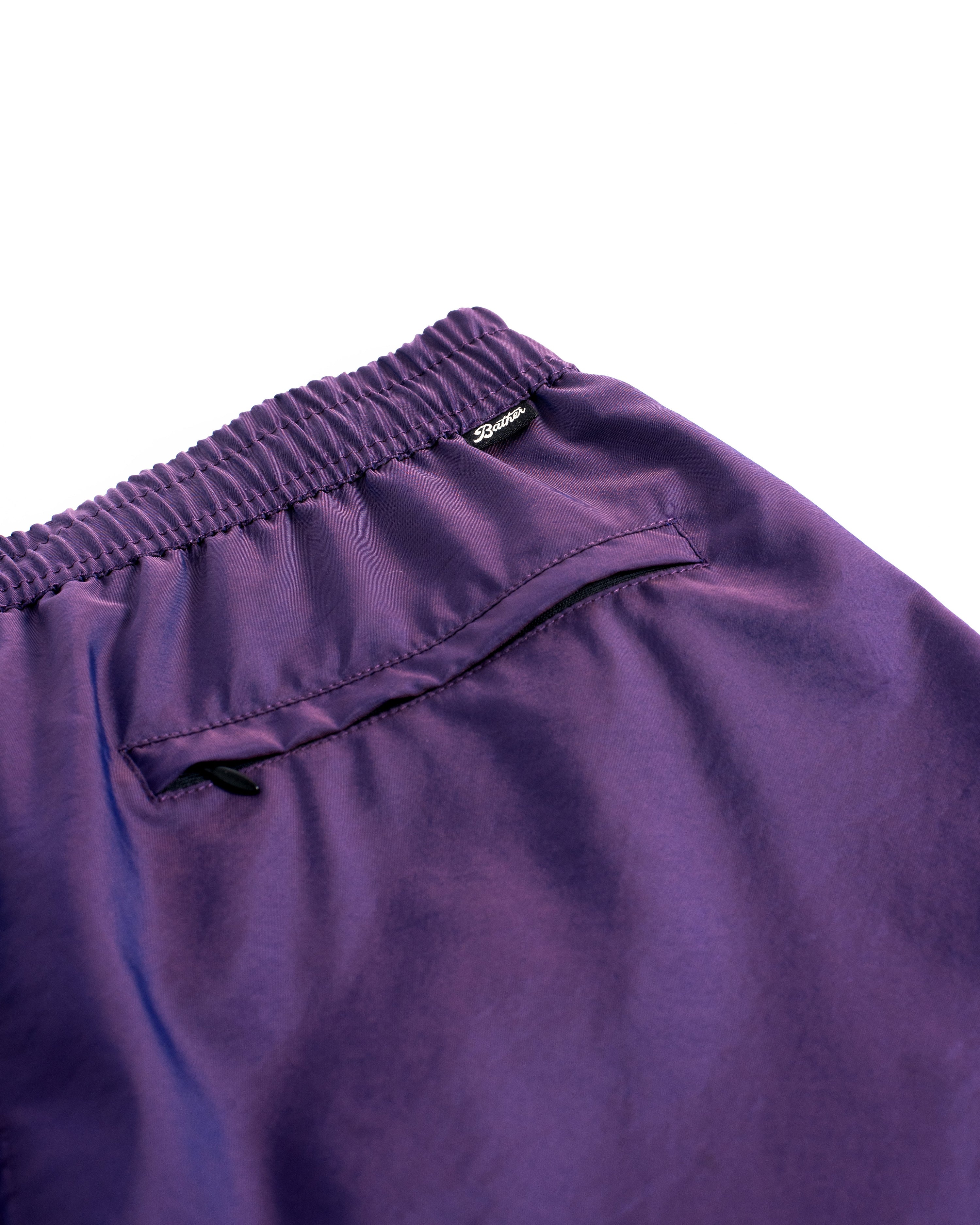 Detail close up view of men's shiny swim trunk in dark purple featuring zipper closure back pocket on white background