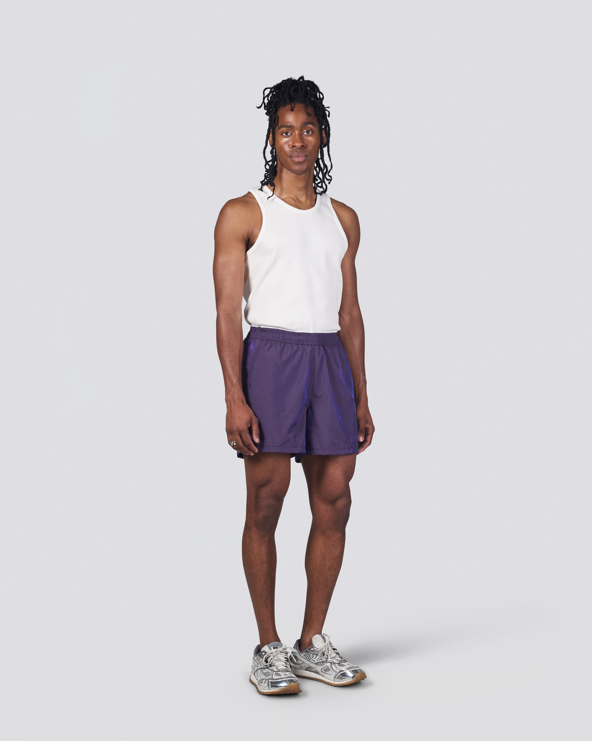 Man in white tank top wearing shiny dark purple swim trunk featuring an elastic drawstring waistband on white background