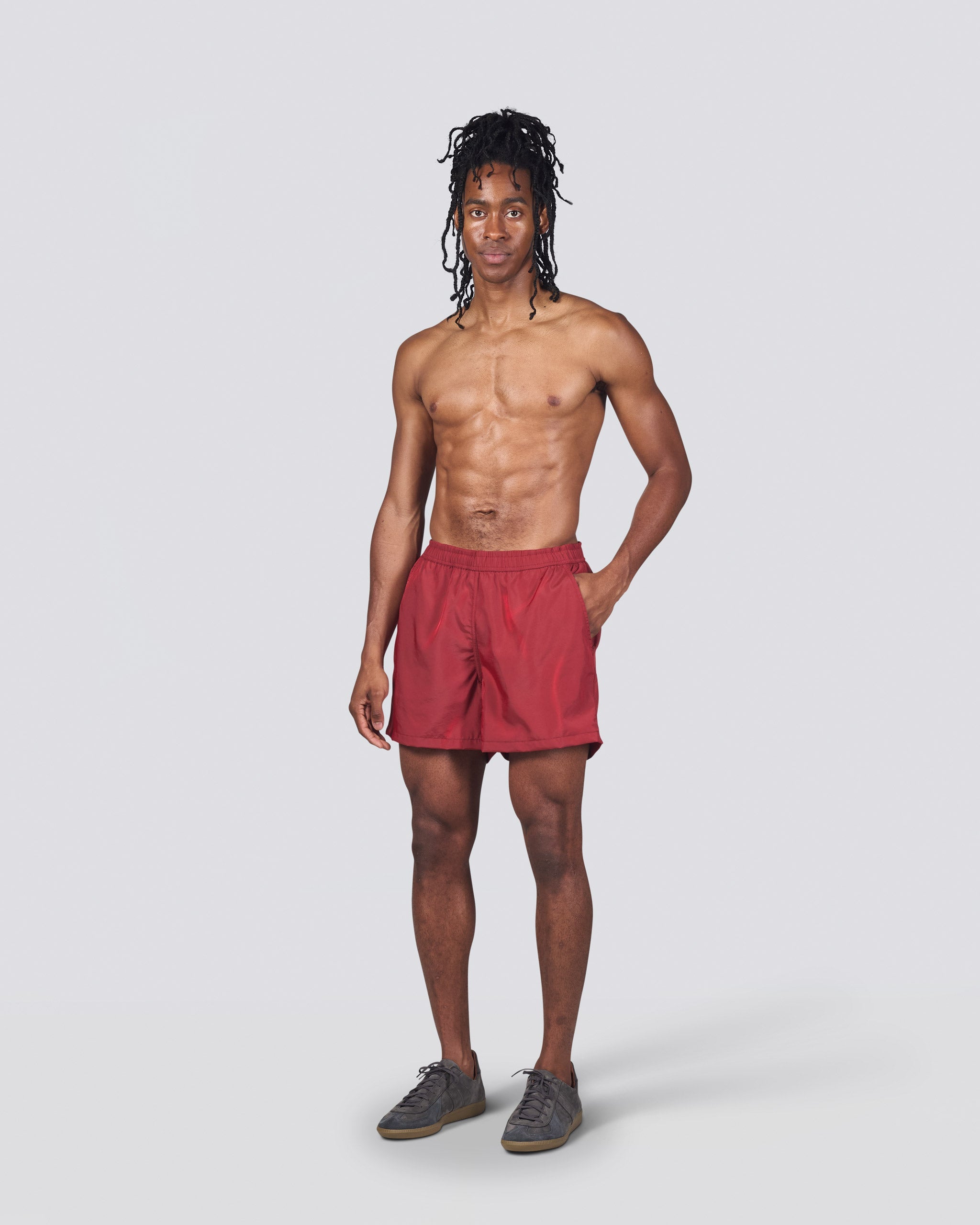 Shirtless man wearing shiny red swim trunk featuring an elastic drawstring waistband on white background