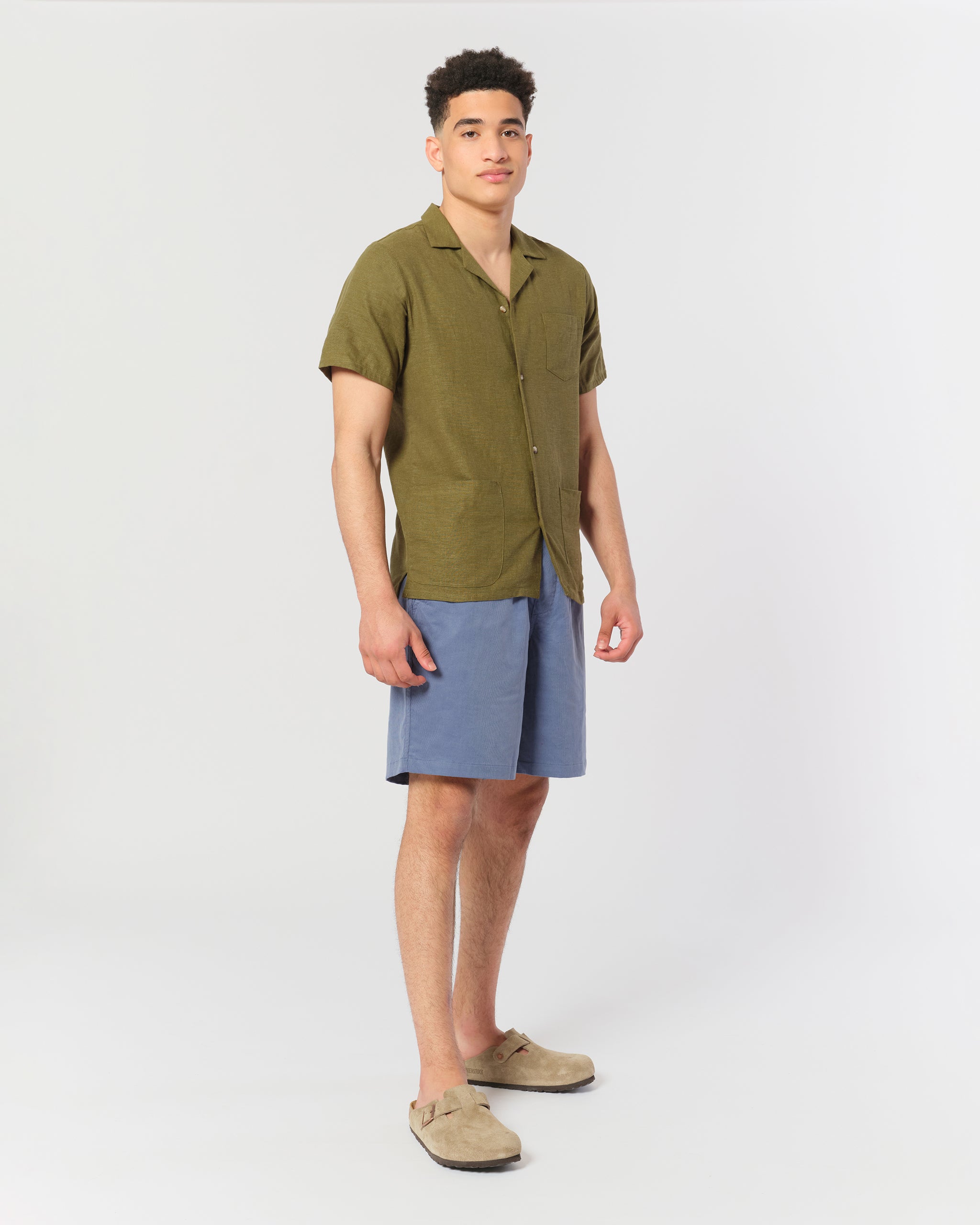 model wearing An olive green linen camp shirt with a chest pocket and two lower pockets on the front