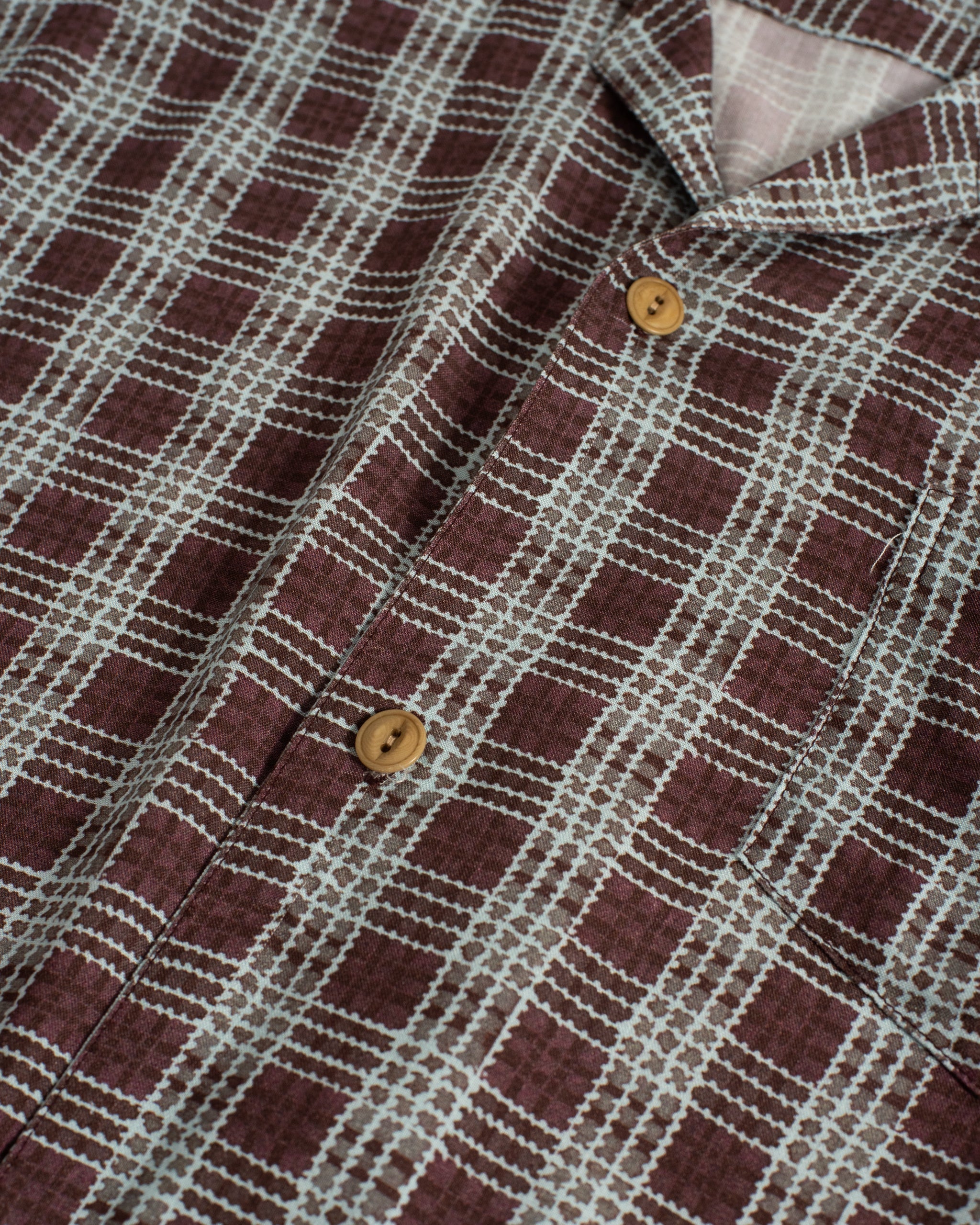 A close-up detail of the Amethyst Tartan Camp Shirt, showing the hand-drawn purple and blue plaid texture and a natural tan Corozo button along the front placket.