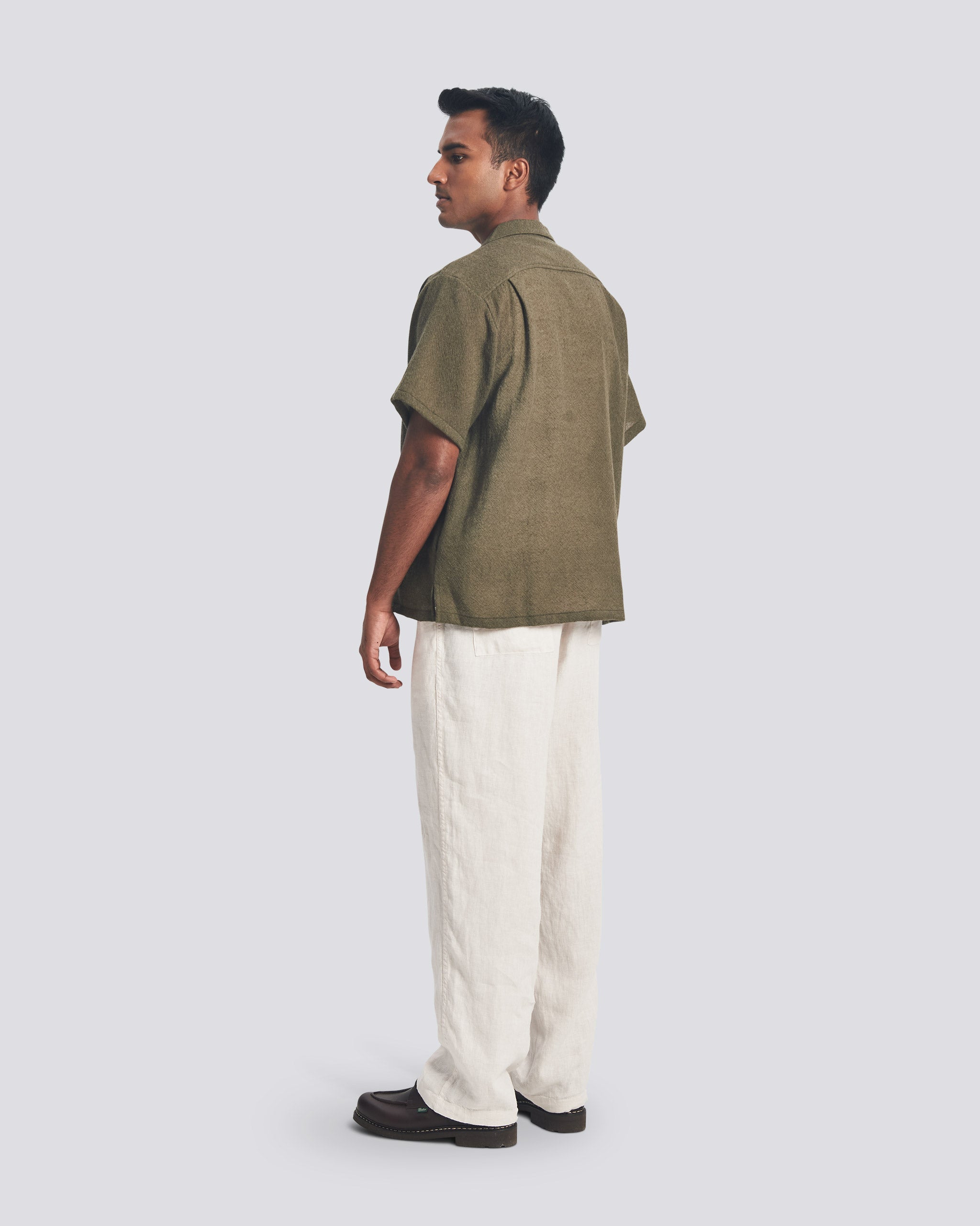 Back view of a model wearing the Bather Men's Army Wool Gauze Camp Shirt, showcasing the dark olive textured Japanese wool gauze and the relaxed, straight-hem silhouette.